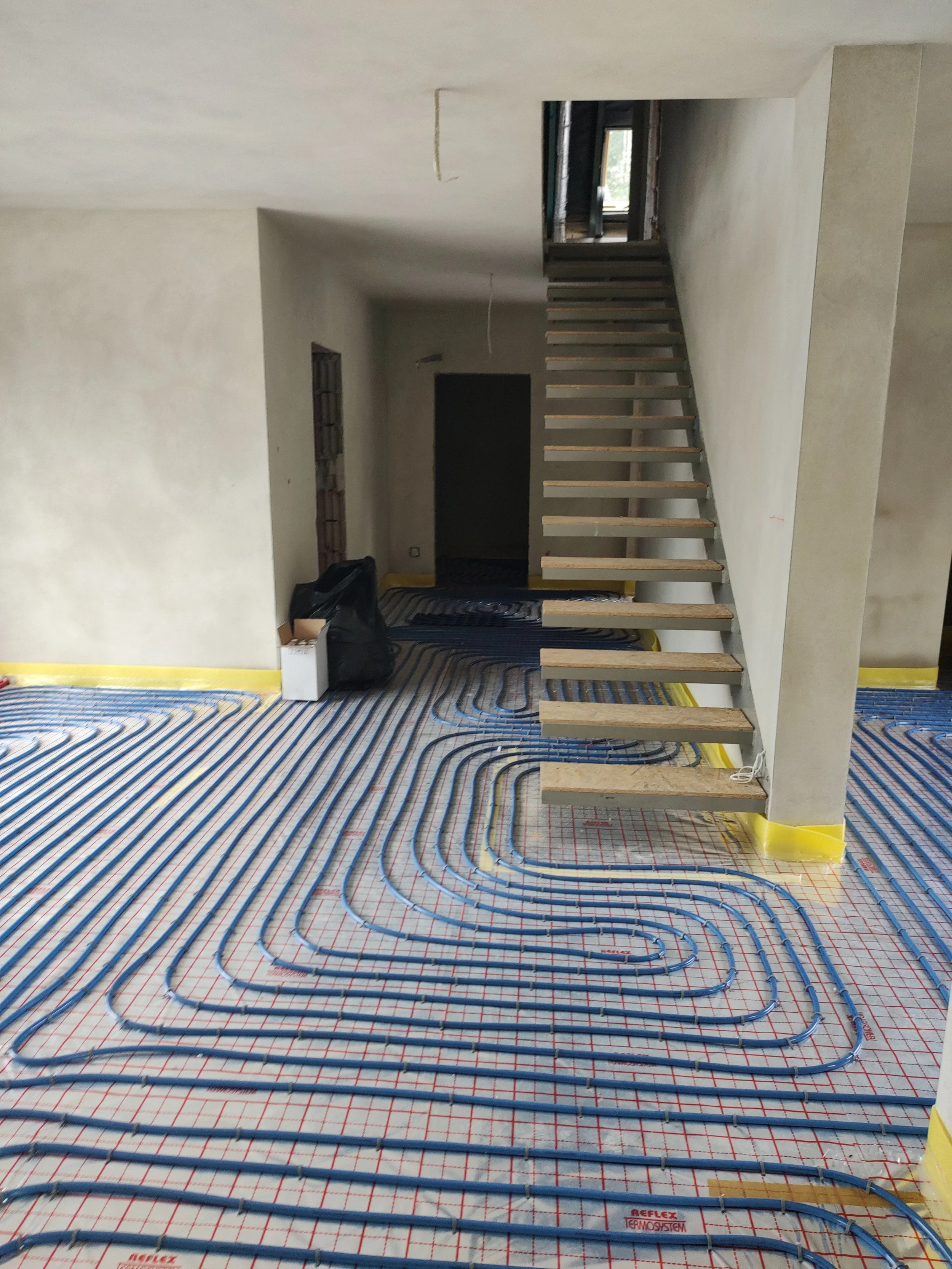 Underfloor heating installation with blue PEX tubing laid in a serpentine pattern on a grid in a room under construction.