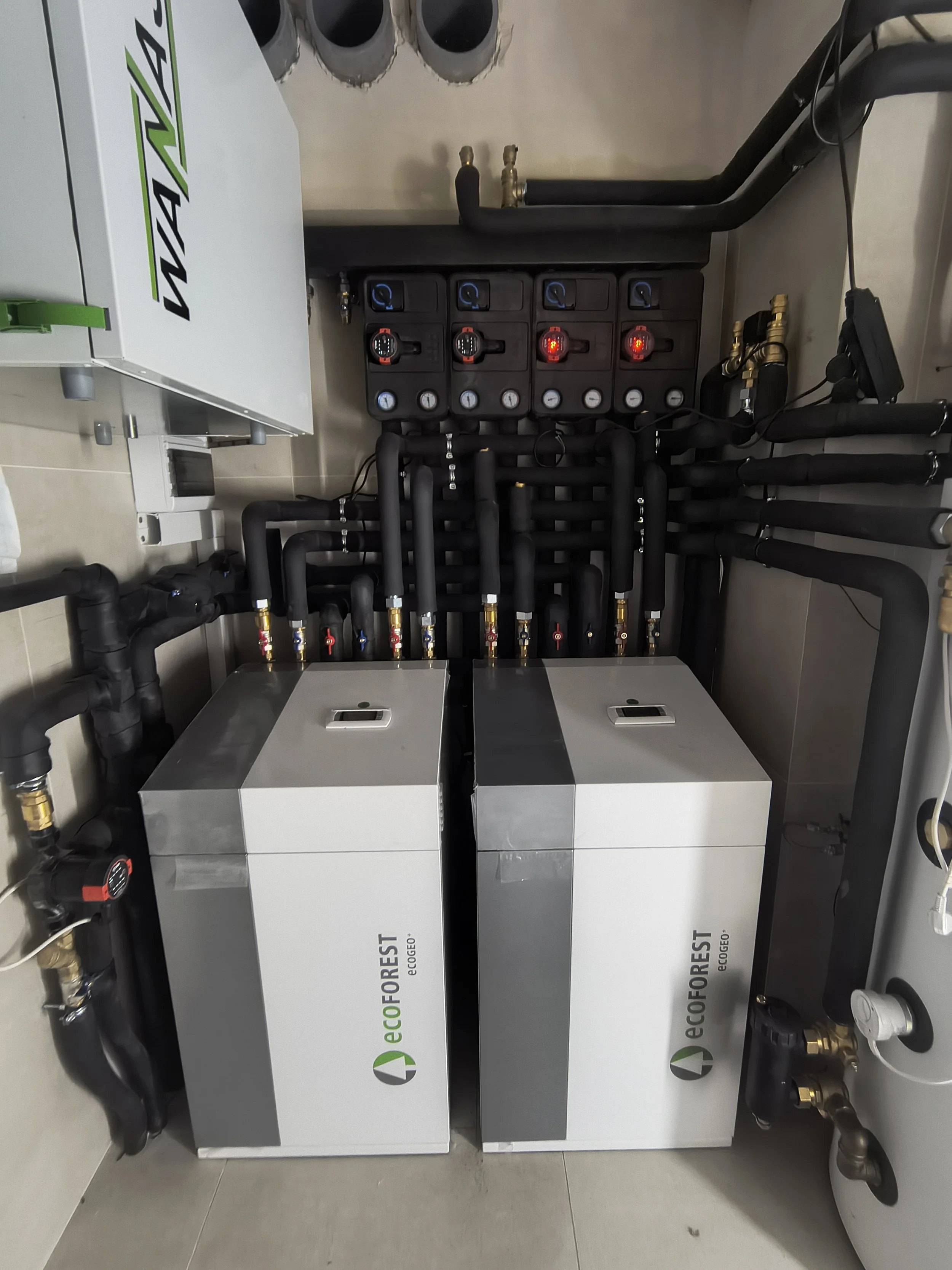 Industrial equipment labeled 'ecoFOREST' with multiple black pipes, gauges, and red indicator lights in a utility room.