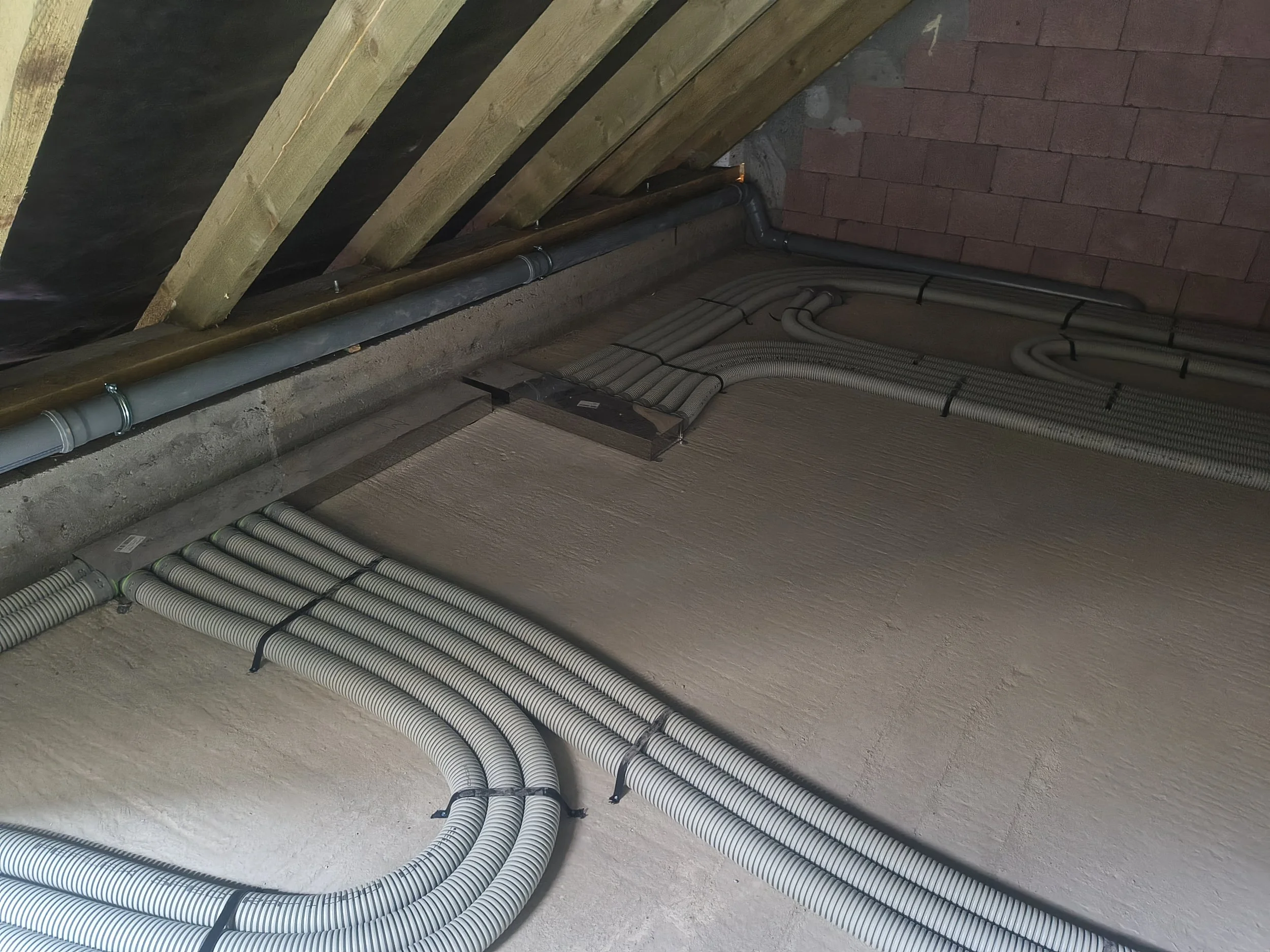 Electrical conduit pipes installed on a ceiling and wall of an attic or basement space.