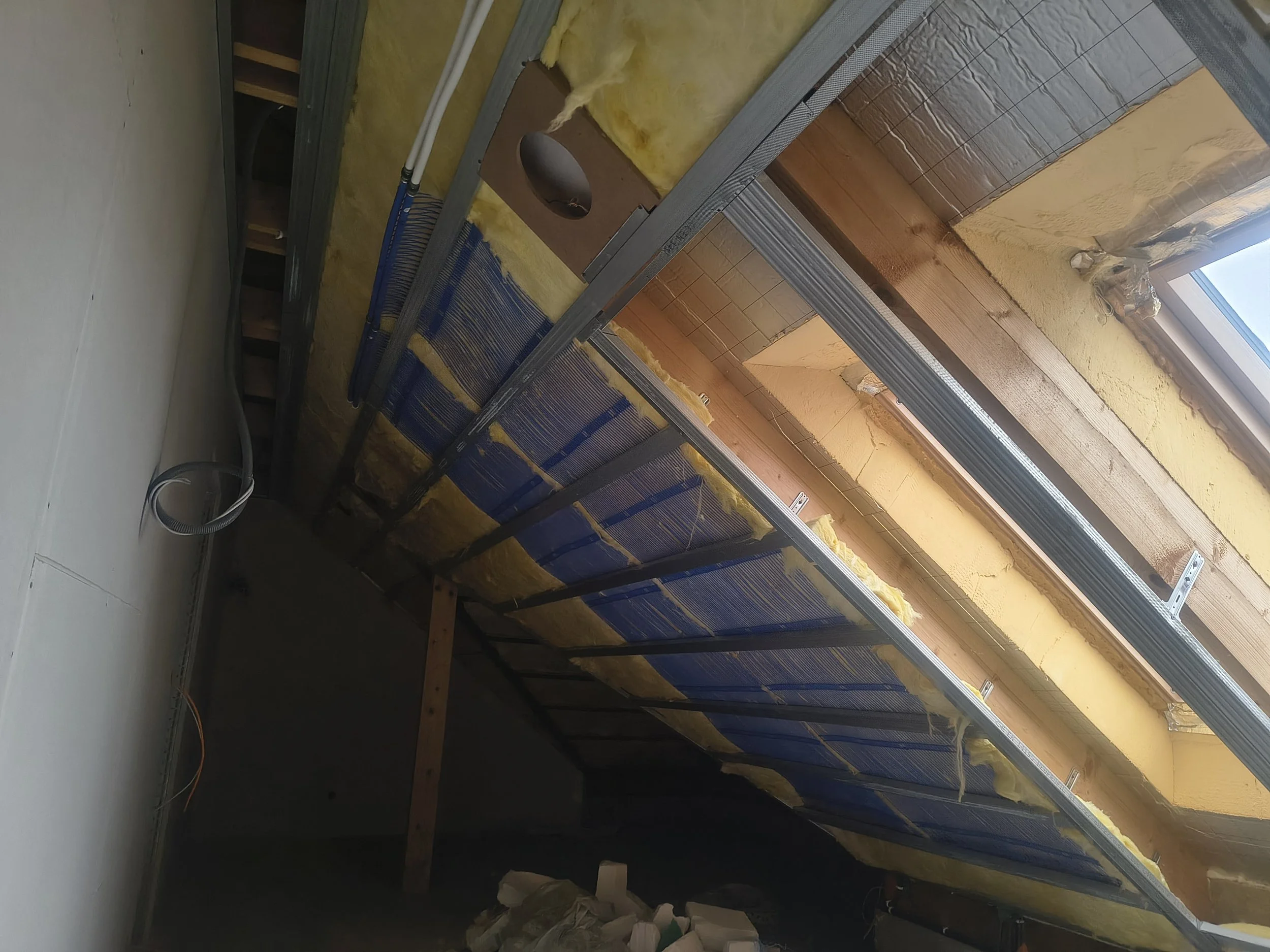 Construction site with insulation and framing for a wall near a window, wires on the floor.
