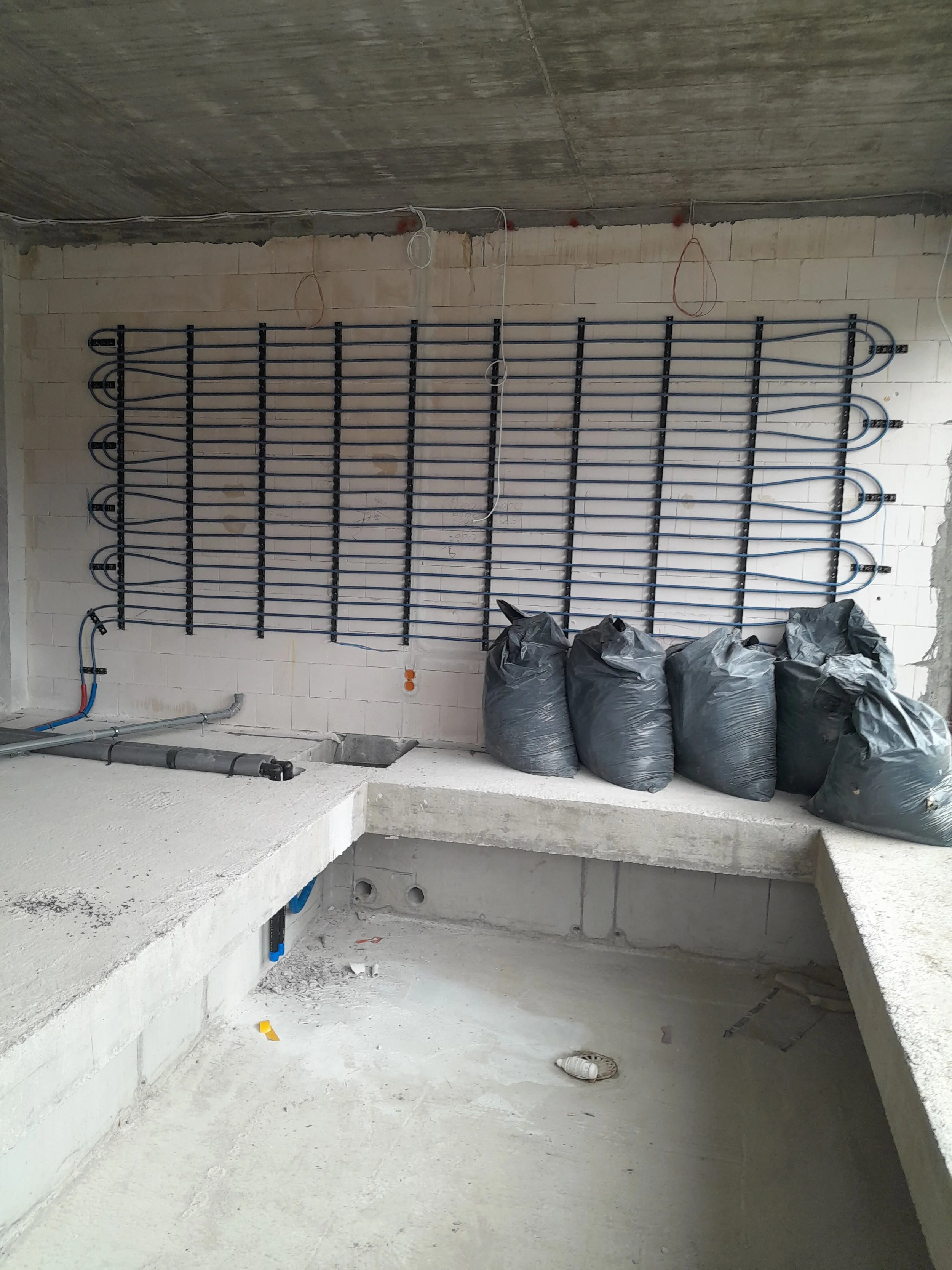 Construction site with concrete walls and floors, electrical wiring, and black plastic bags filled with materials placed along the wall.