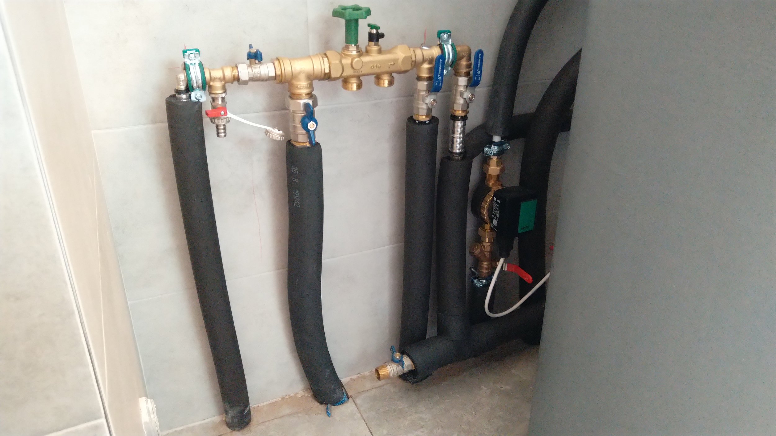 Installation of water pipes with insulation and valves against a wall in a building utility area.