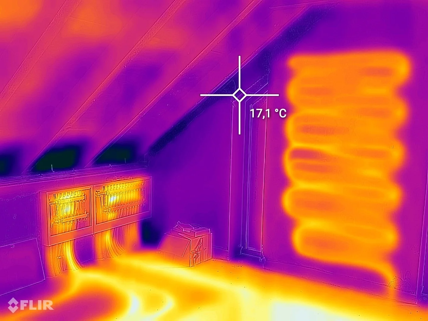 Infrared image of an attic corner showing electrical panels, wooden beams, insulation, and a wall with a temperature reading of 17.1°C.