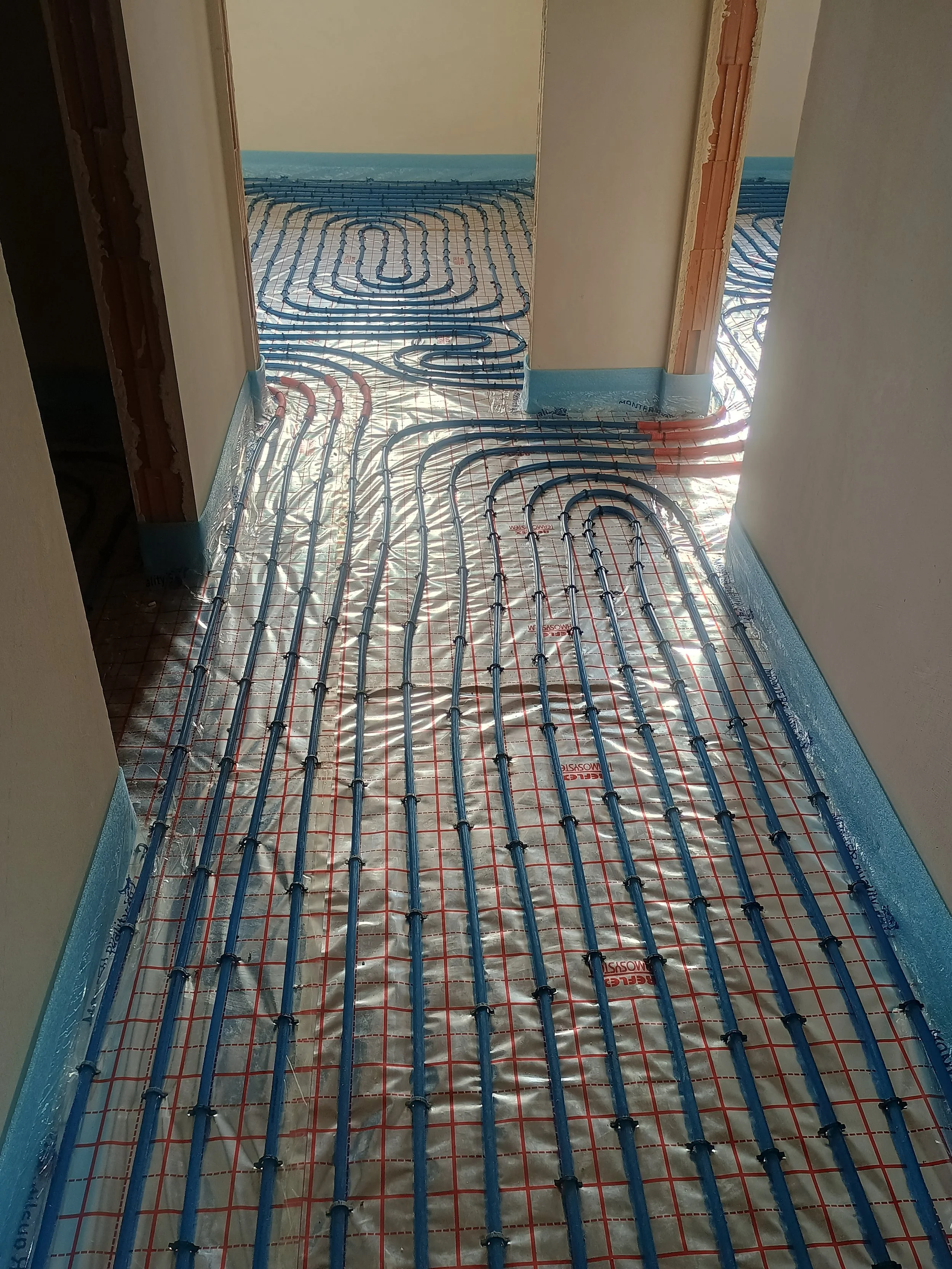 Underfloor heating pipes installed in a building under construction, with reflective insulation underneath, and partially finished walls.