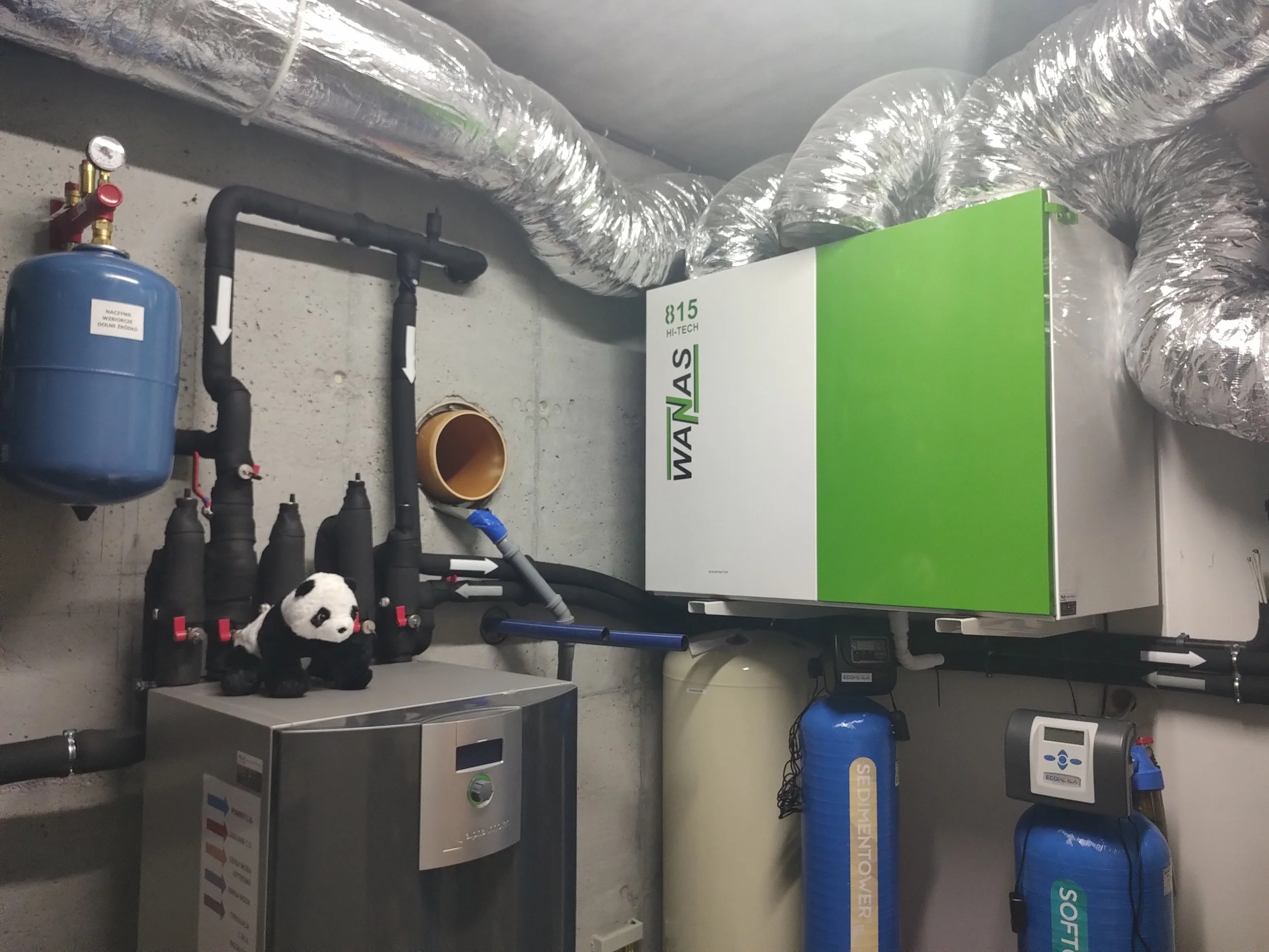 Industrial HVAC system with ductwork, pipes, control panels, and a plush panda toy on a metal cabinet.