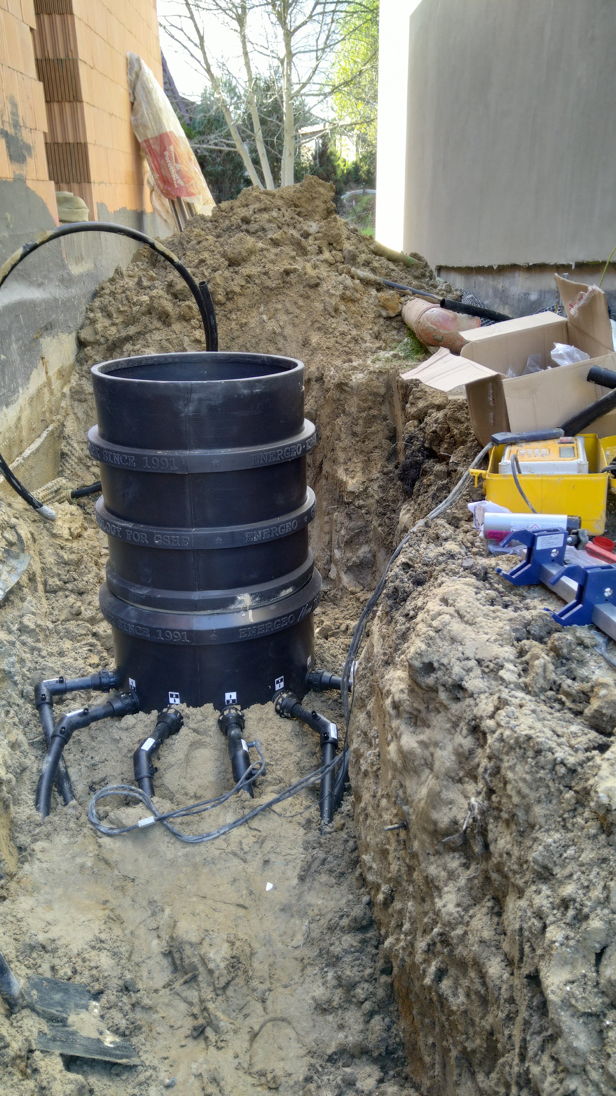 Underground construction site with a large black plastic pipe, plumbing and electrical wiring, surrounded by dirt and soil, with construction tools and boxes on the side.