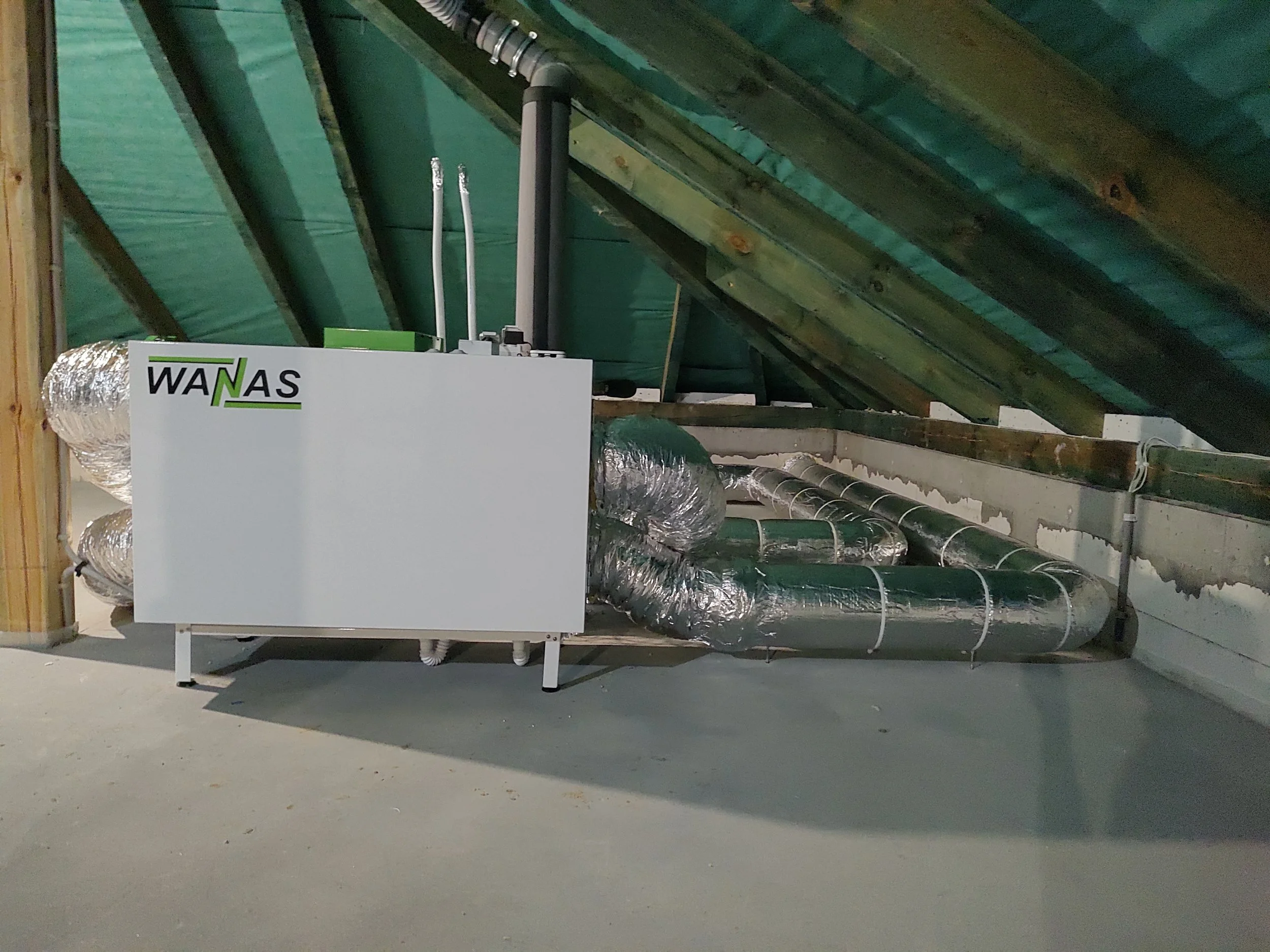 HVAC system installation in an unfinished basement with green insulation and metal ducts.