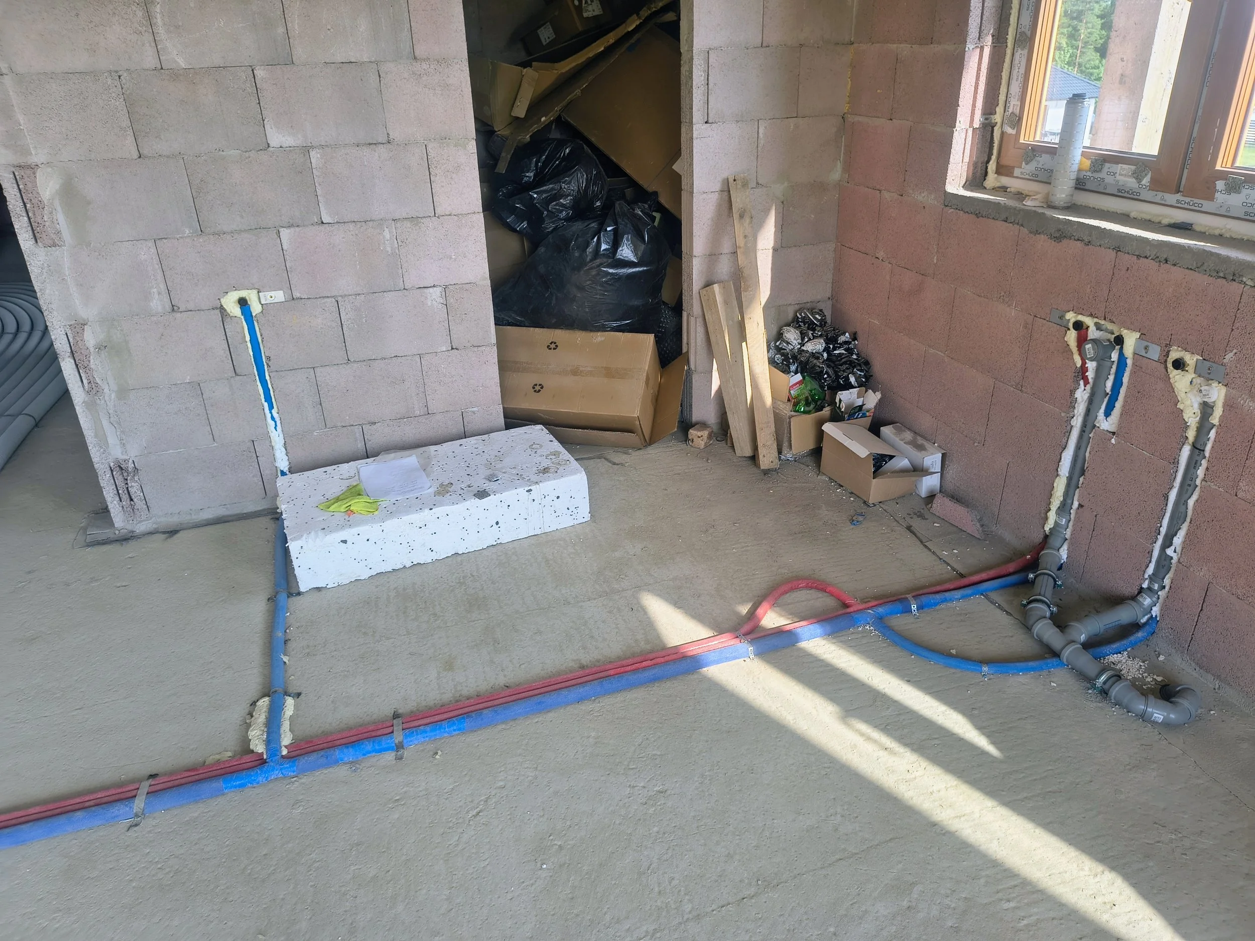Interior of a building under construction with exposed brick walls, construction materials, and plumbing pipes visible.