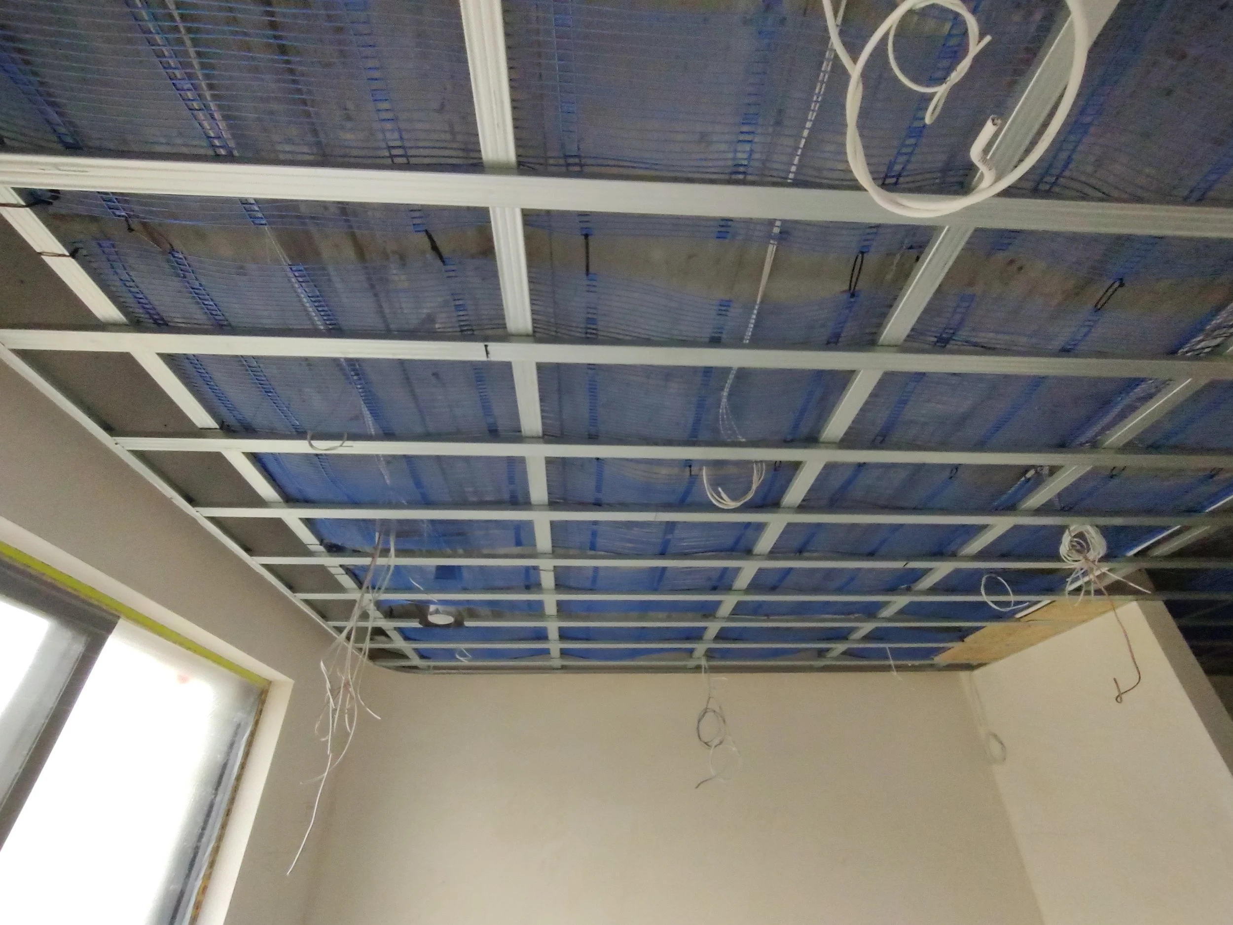 Ceiling of a room under construction with a metal grid framework and exposed electrical wires.