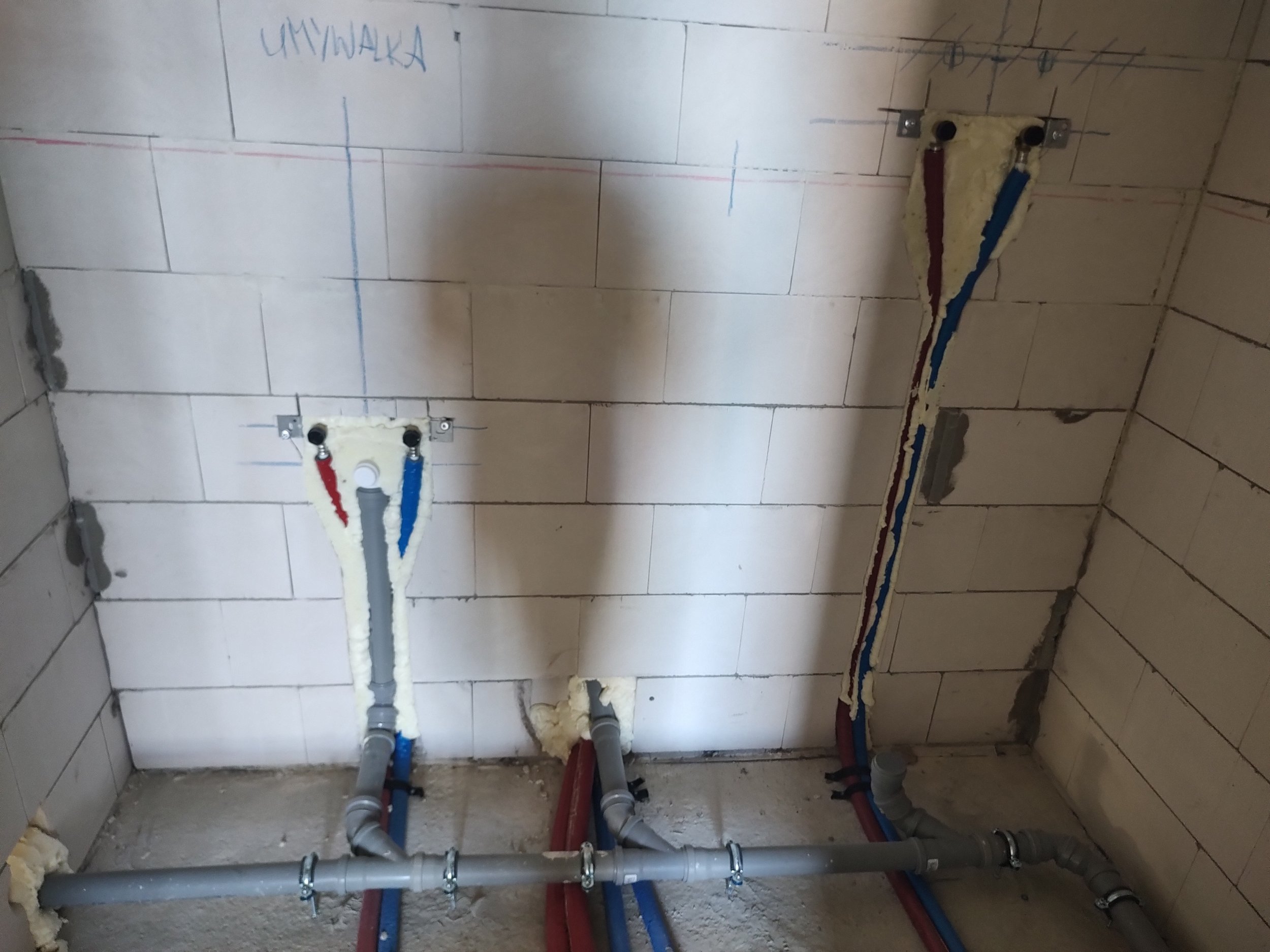 Plumbing pipes and fixtures installed in a wall with tile, with markings and labels for a bathroom or kitchen.