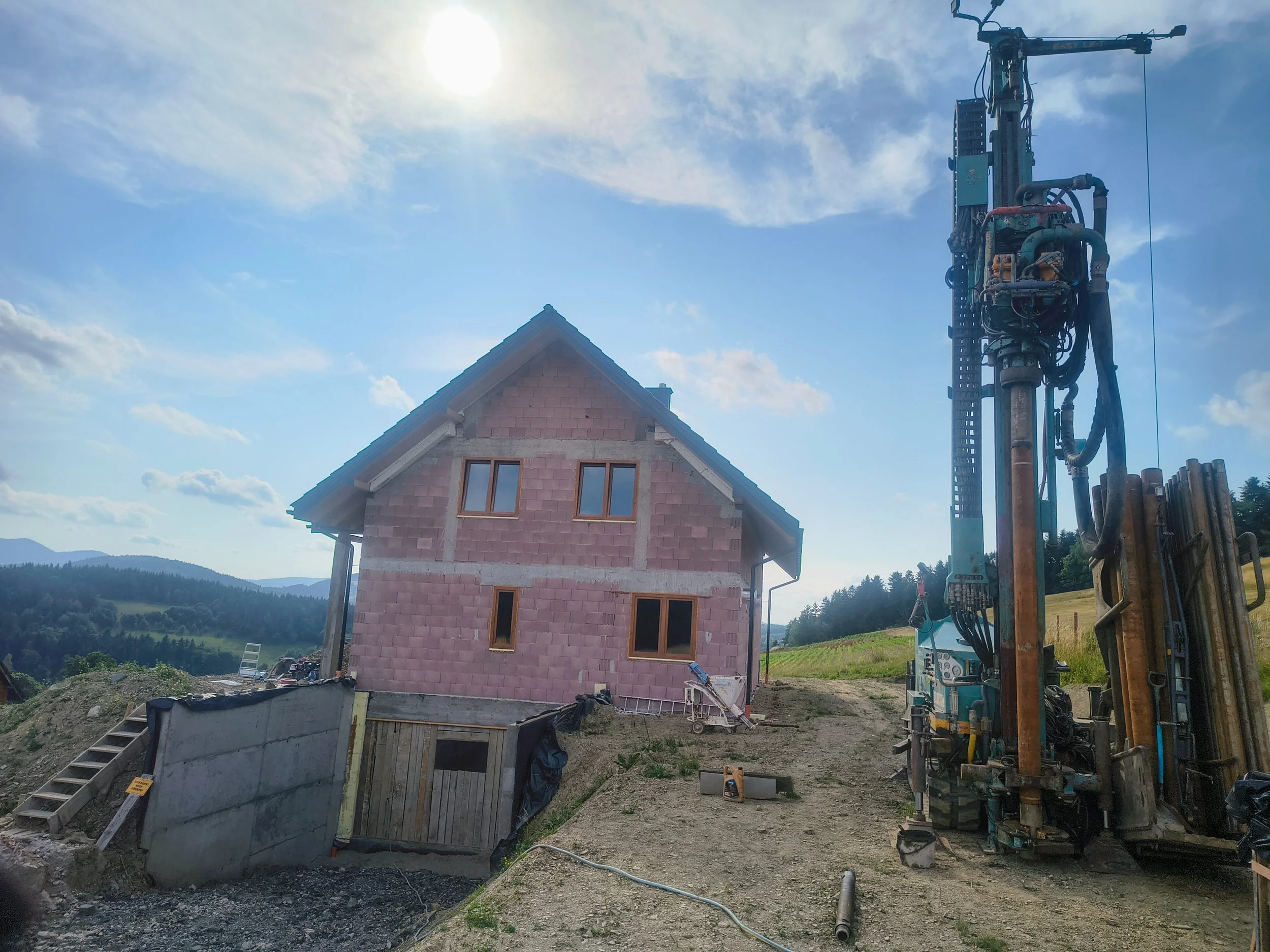 Construction site with a house under construction, construction equipment, and a partly cloudy sky.