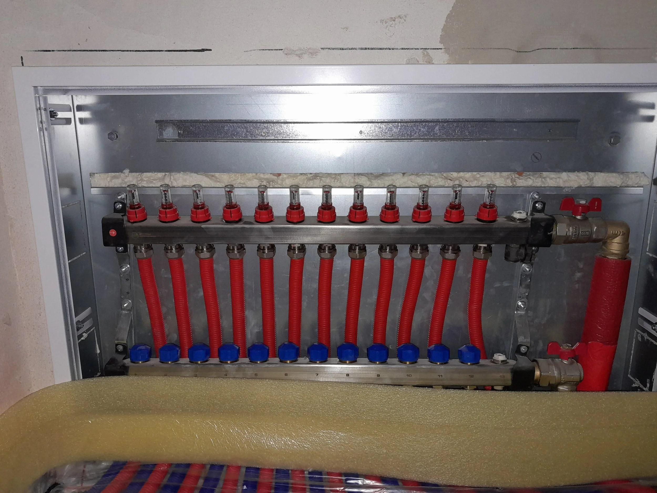 An electrical panel with red and blue valves and hoses, some insulation foam, and metal components.