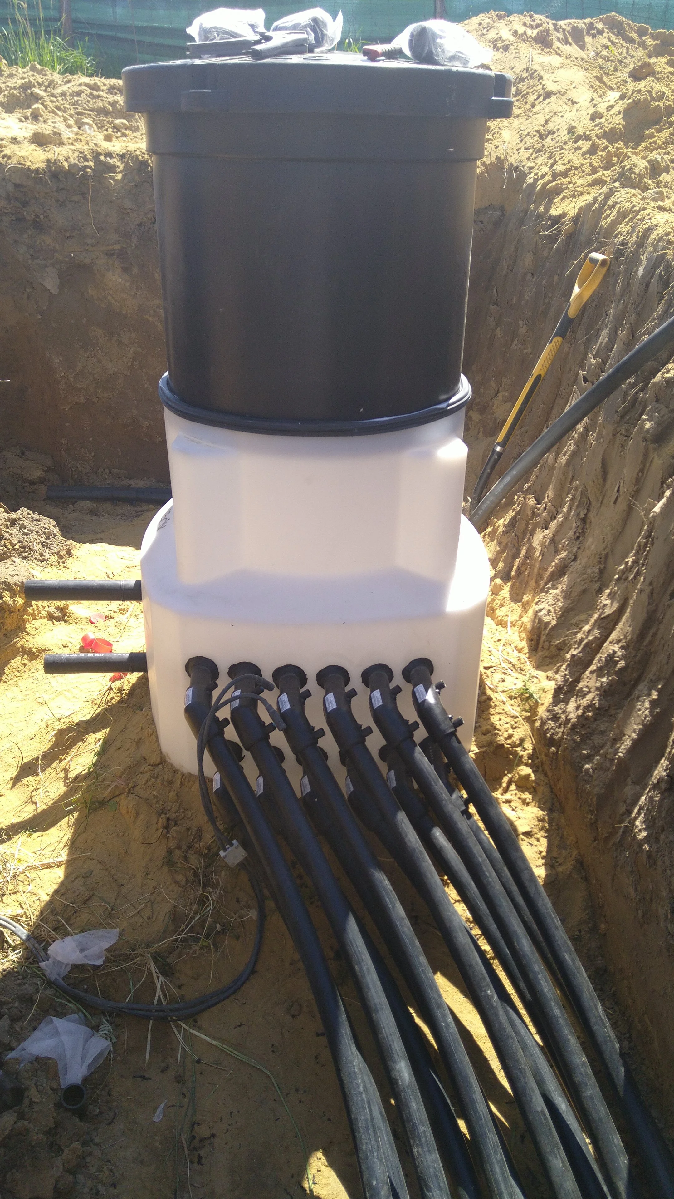 Underground utility box with multiple black cables incoming and outgoing, installed in a dirt excavation site.