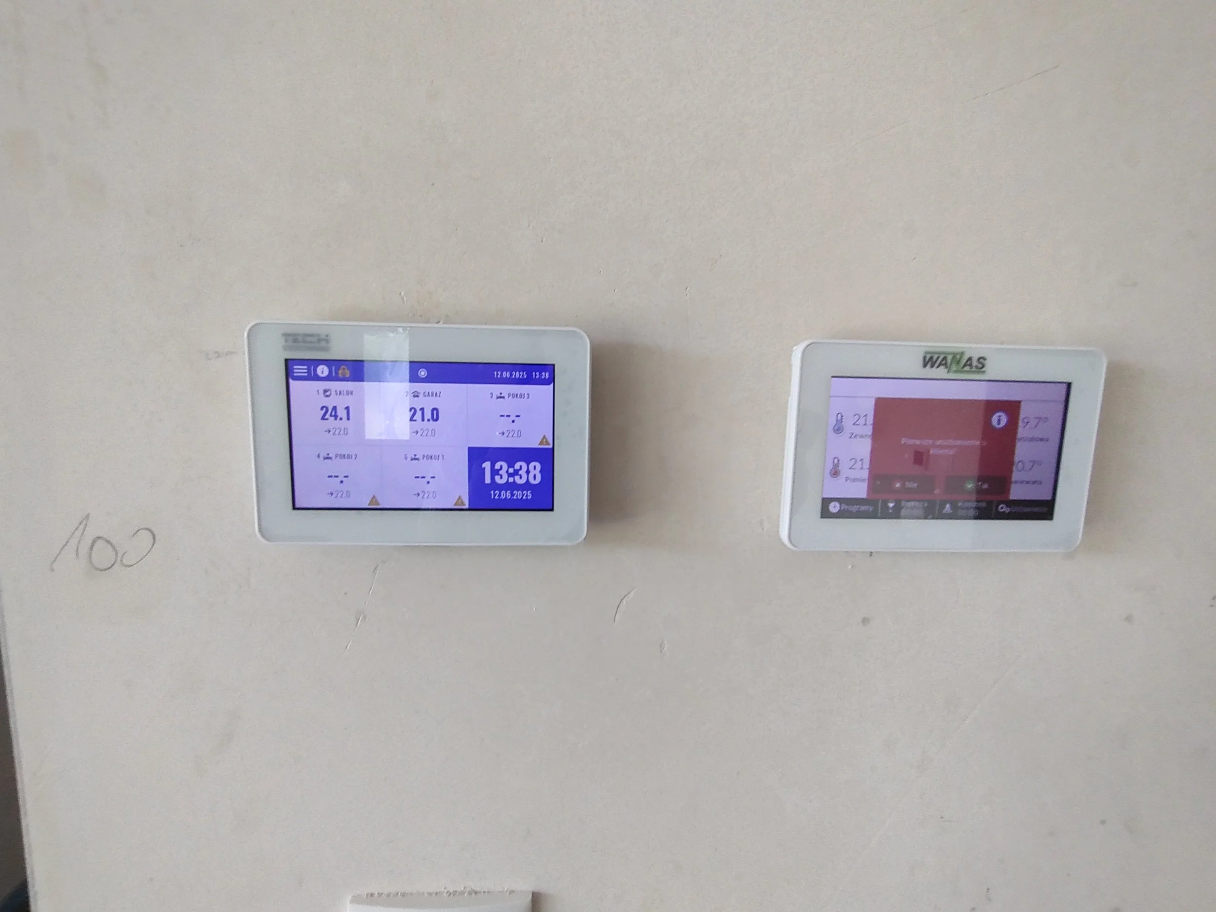 Two digital screens mounted on a wall, displaying information, with some handwritten notes and markings on the wall nearby.