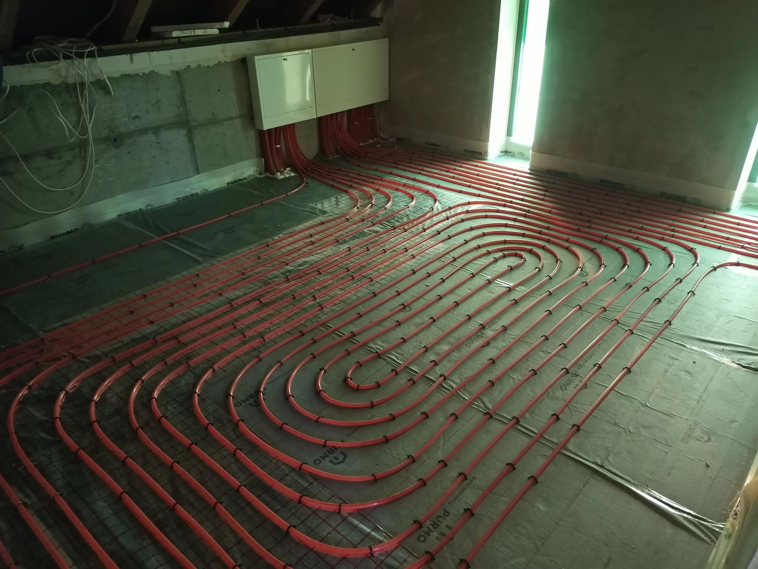 Electrical wiring and pipes installed along a floor with insulation panels in an unfinished room under construction.
