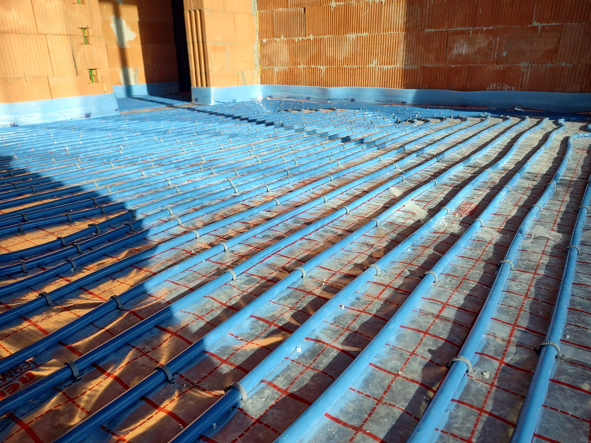 Underfloor heating pipes installed on a wooden subfloor in a building under construction.