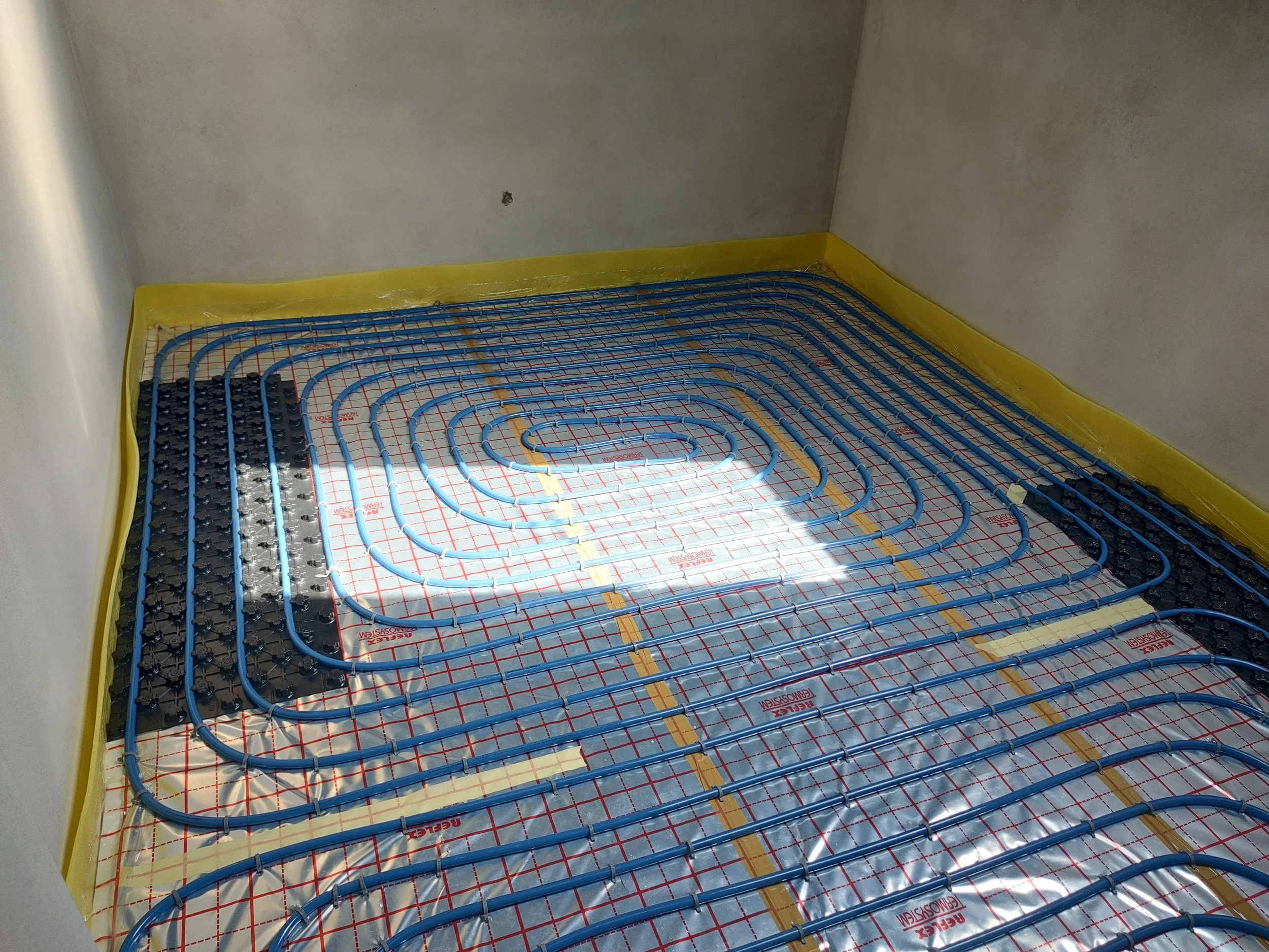 Underfloor heating pipes installed on the floor with yellow edge padding and insulation