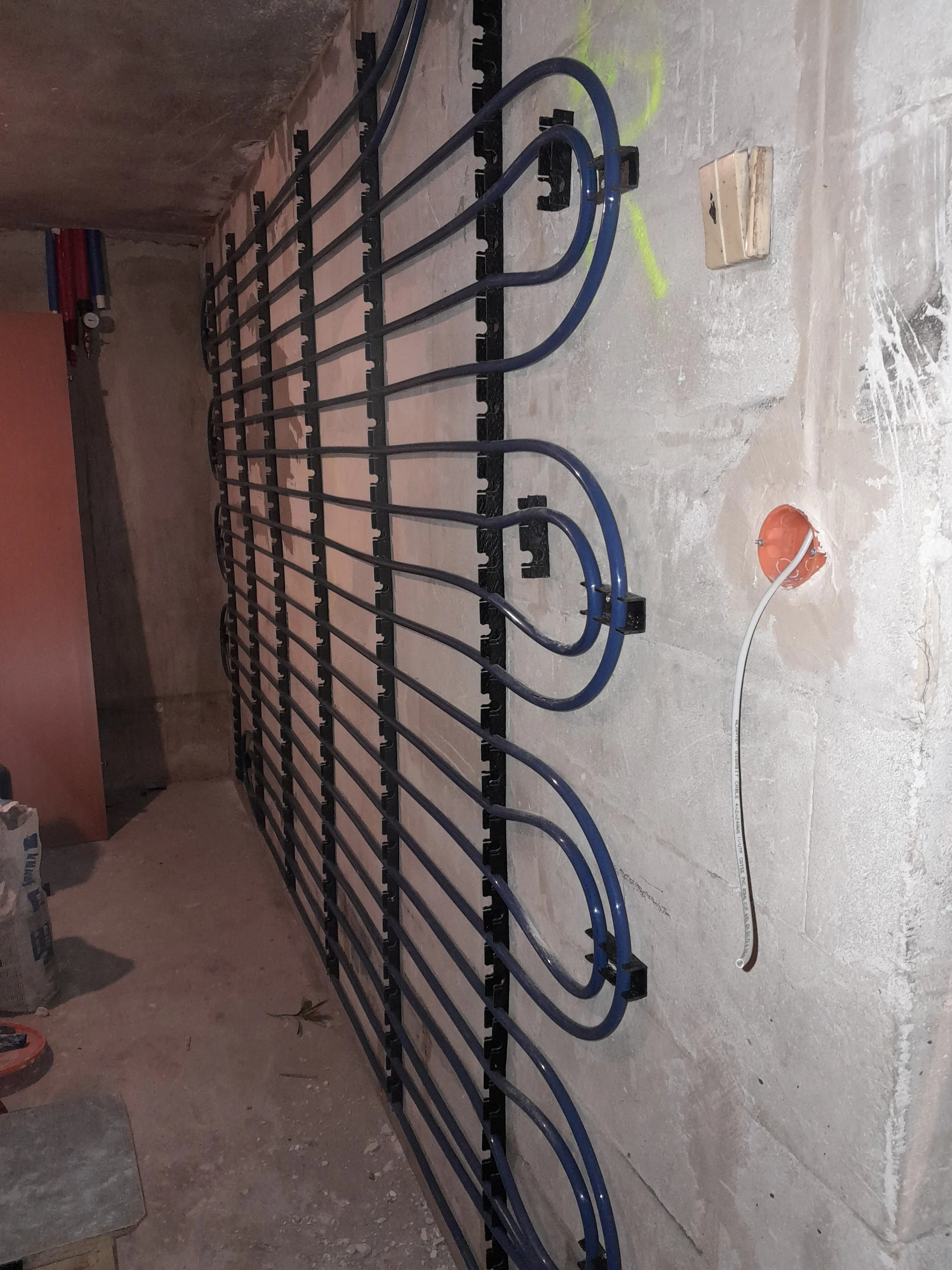 A black metal ramp with blue handlebars for wheelchair access, installed indoors on a concrete floor, with yellow markings and visible electrical wiring on the wall.