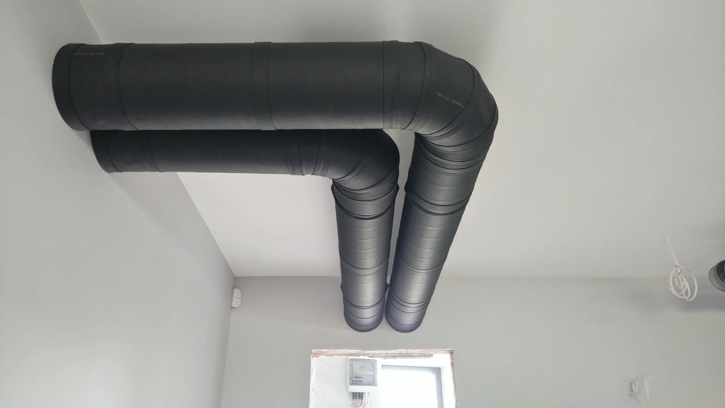 Black industrial HVAC pipes running along the ceiling of a white room.