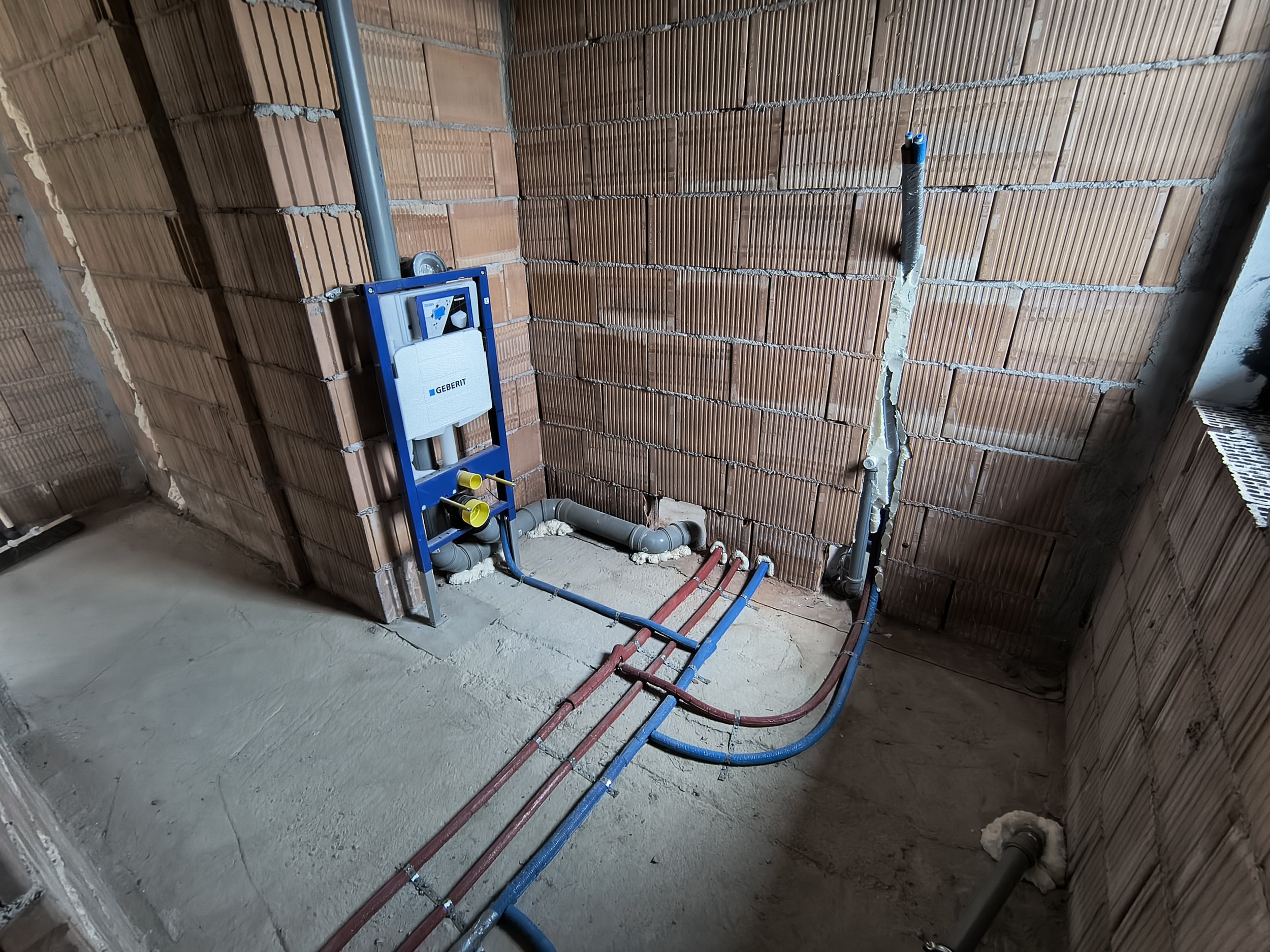 Interior of a building under construction with exposed brick walls, plumbing pipes, and electrical wiring.