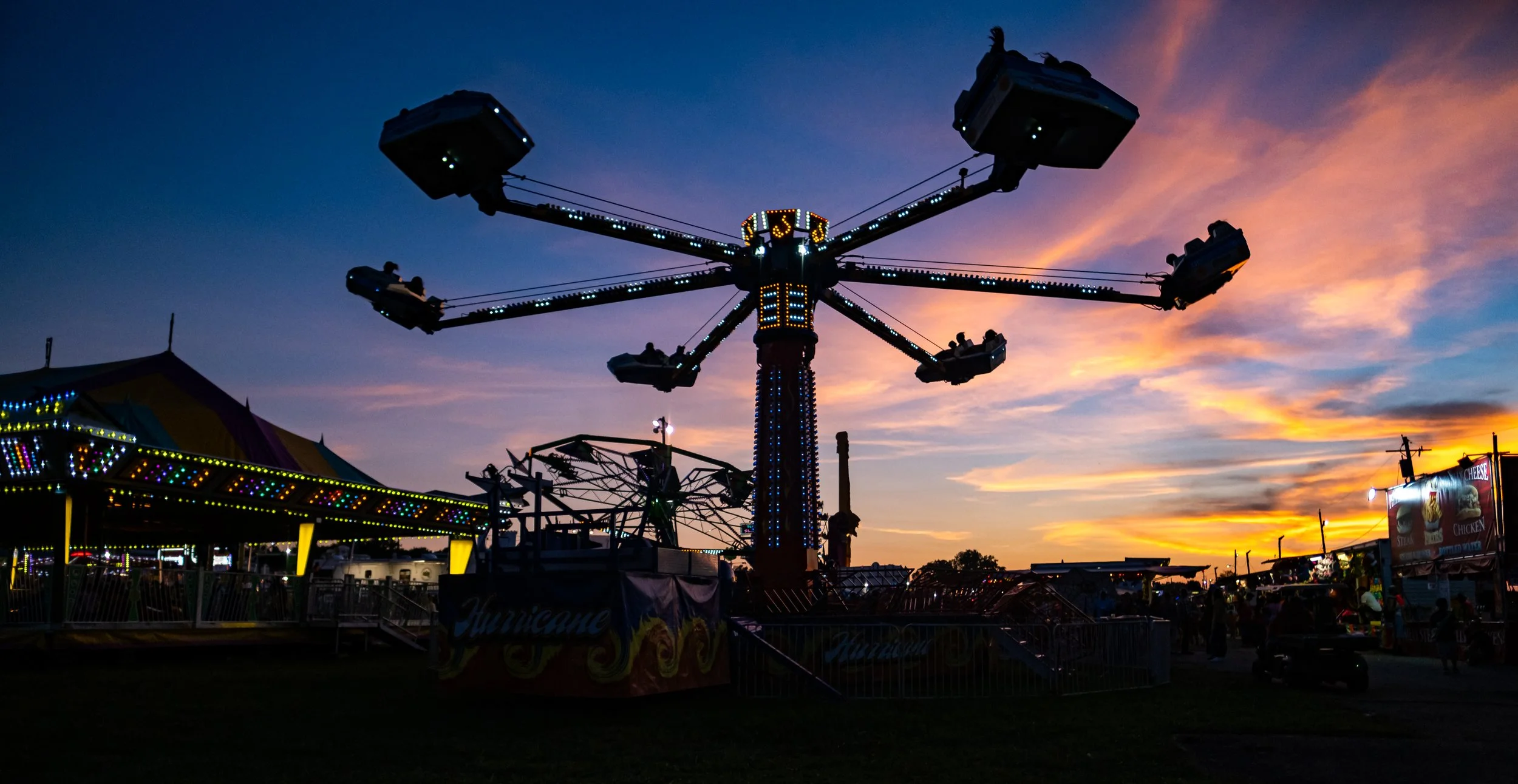 An amusement park ride at sunset with a large spinning swing ride and colorful lights.