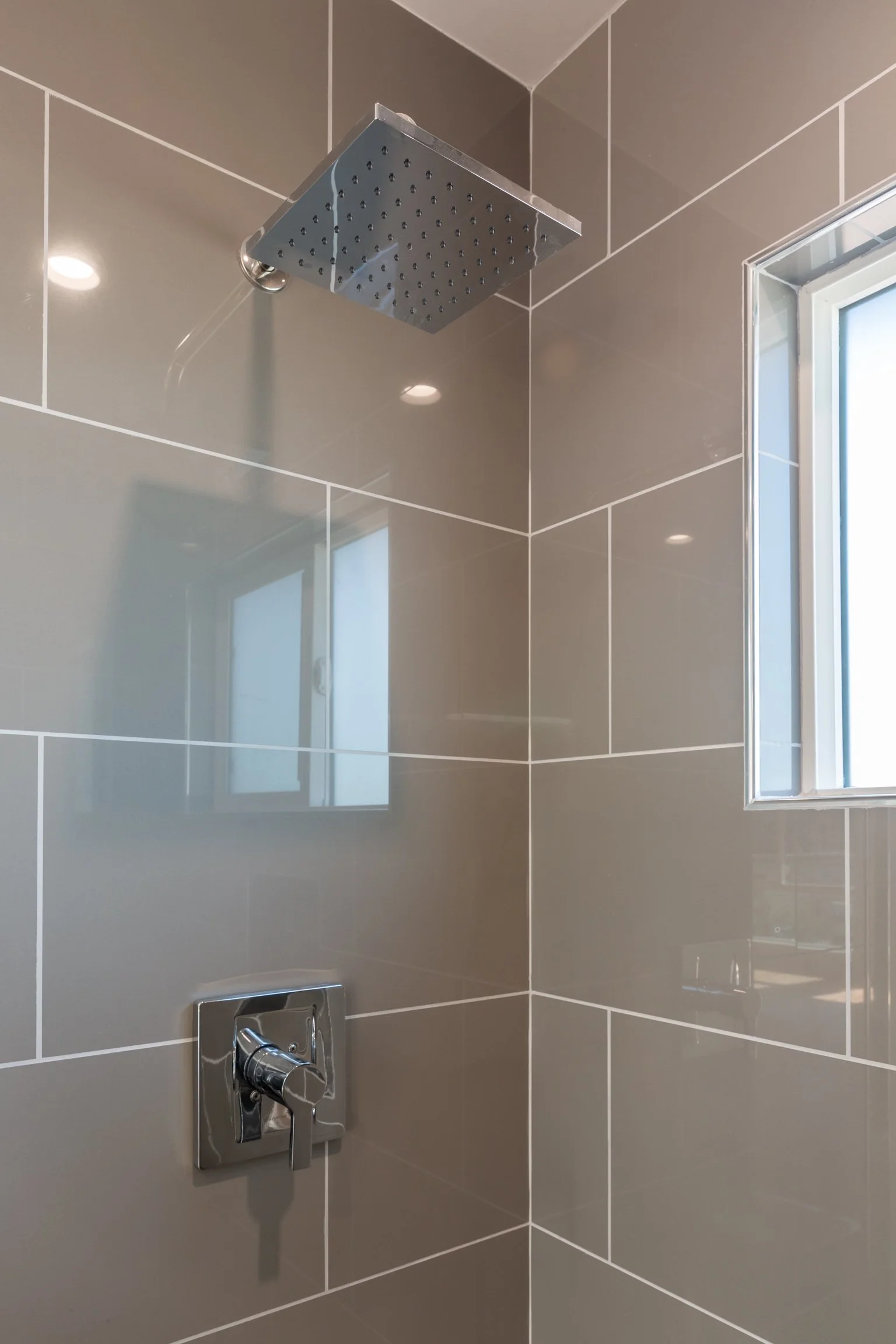 Close-up of a modern shower with a square rain showerhead attached to a tiled wall, and a chrome shower control handle beneath.