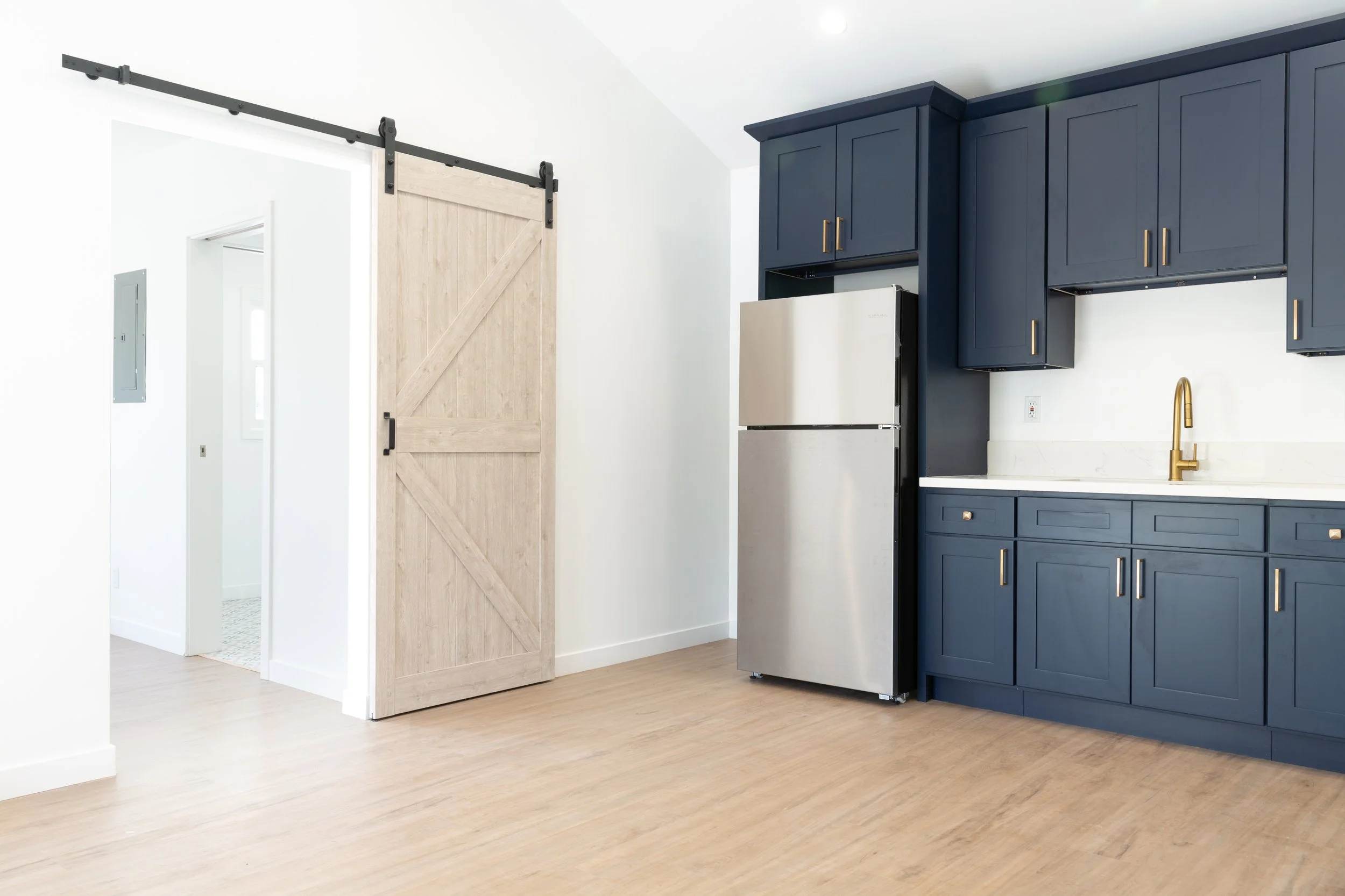 Modern kitchen with navy blue cabinets, a gold faucet, a stainless steel refrigerator, and a sliding barn door with black hardware.
