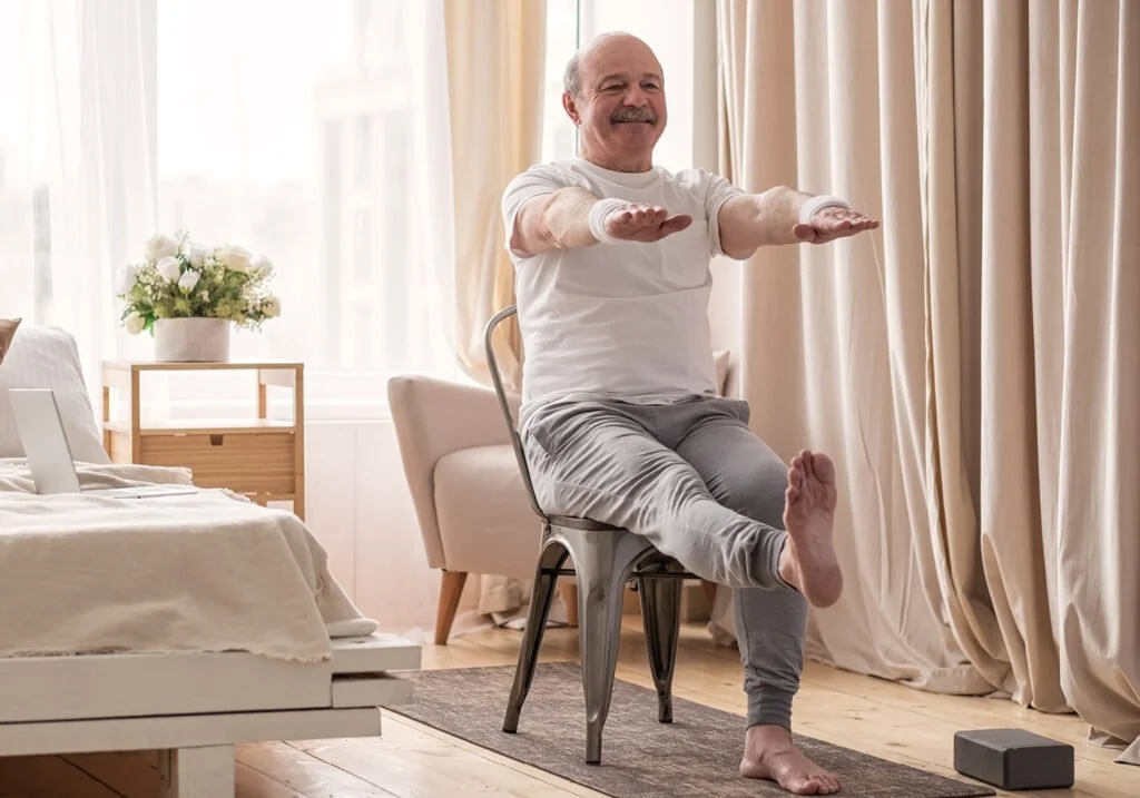 Elderly man practicing seated yoga in a bright living room