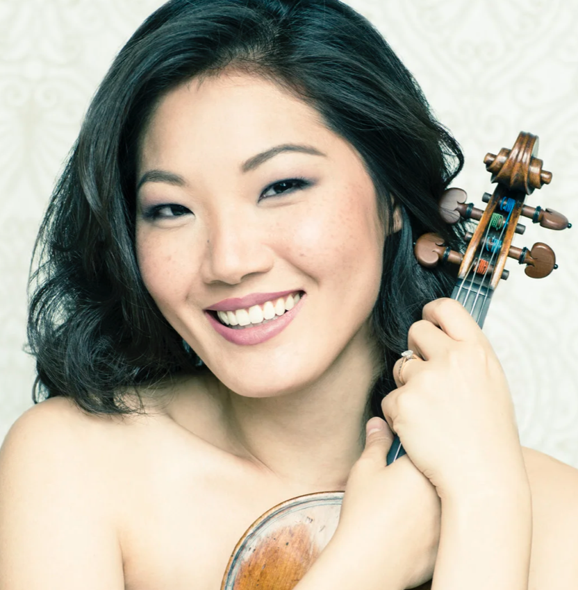 A woman smiling and holding a violin close to her face.