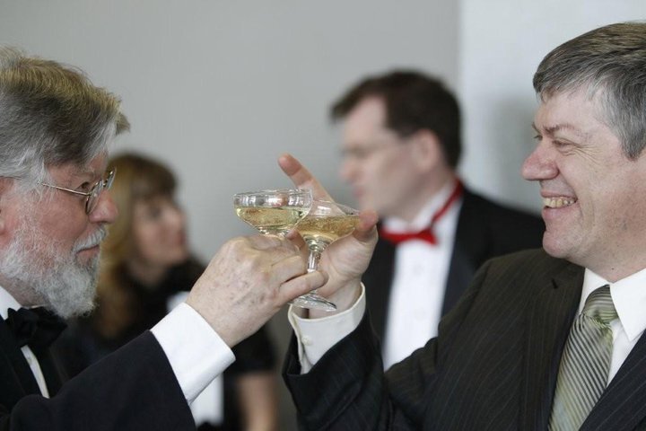 Two men in formal attire clinking champagne glasses at a social gathering.