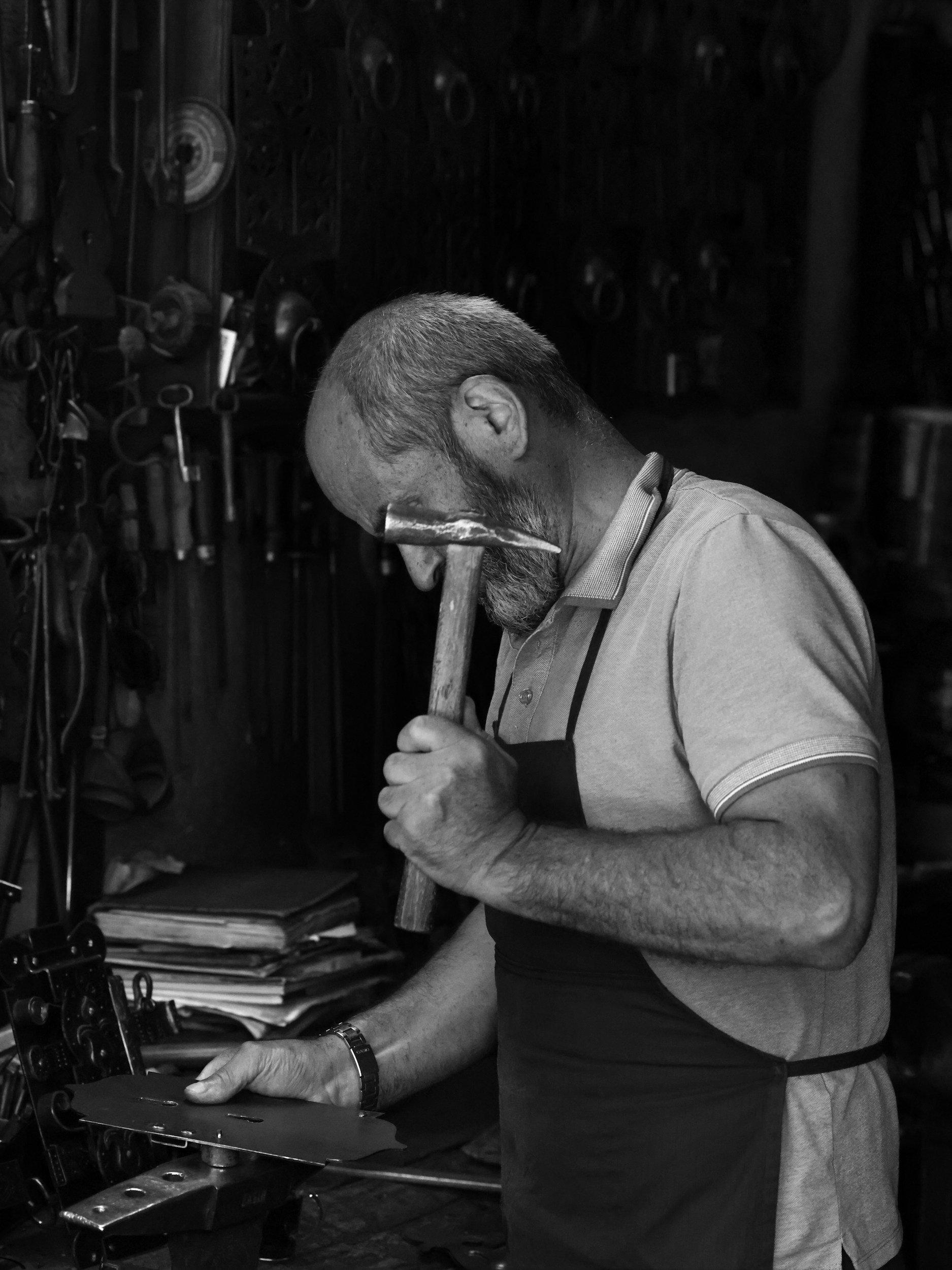 Man with a beard and short hair, wearing a uniform, working with tools in a workshop filled with mechanical and hardware equipment.