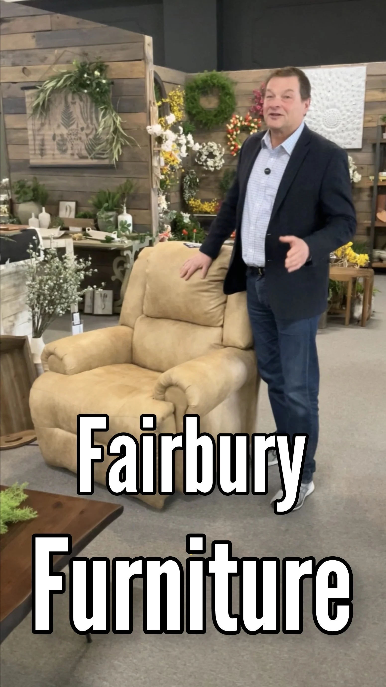 Man standing next to beige armchair in furniture store with wooden wall and various decorative items and plants in background.