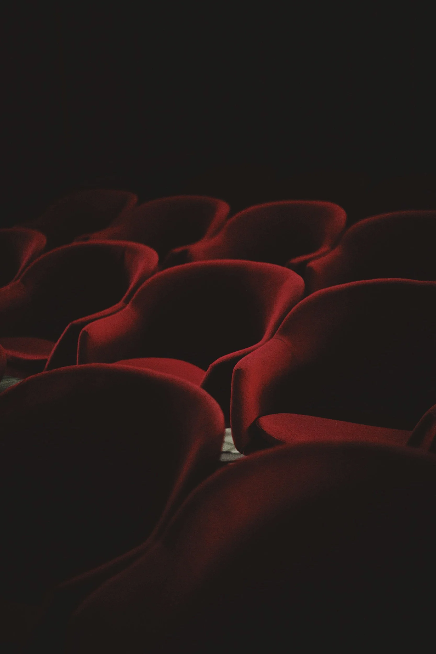 Empty red theater seats in a dark theater.