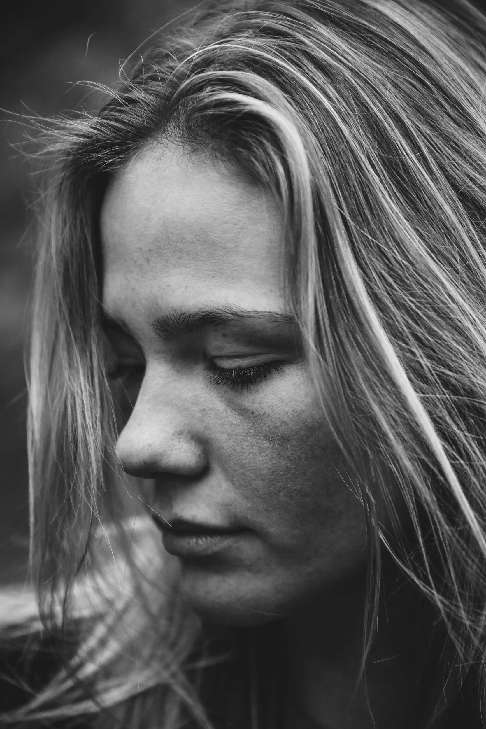 Close-up black and white photograph of a woman's face with her eyes closed, partially obscured by her long, flowing hair.