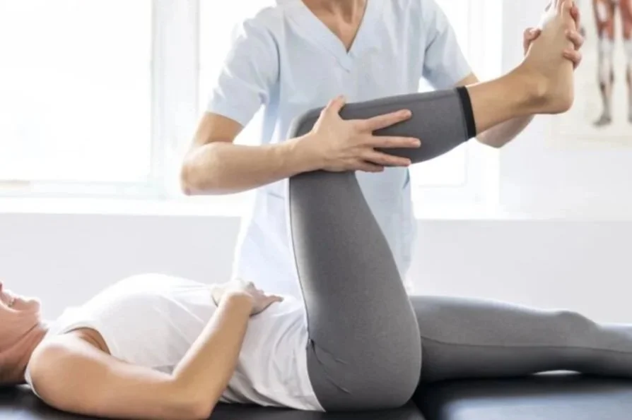 Physical therapist assists a patient with leg exercise in a clinic.
