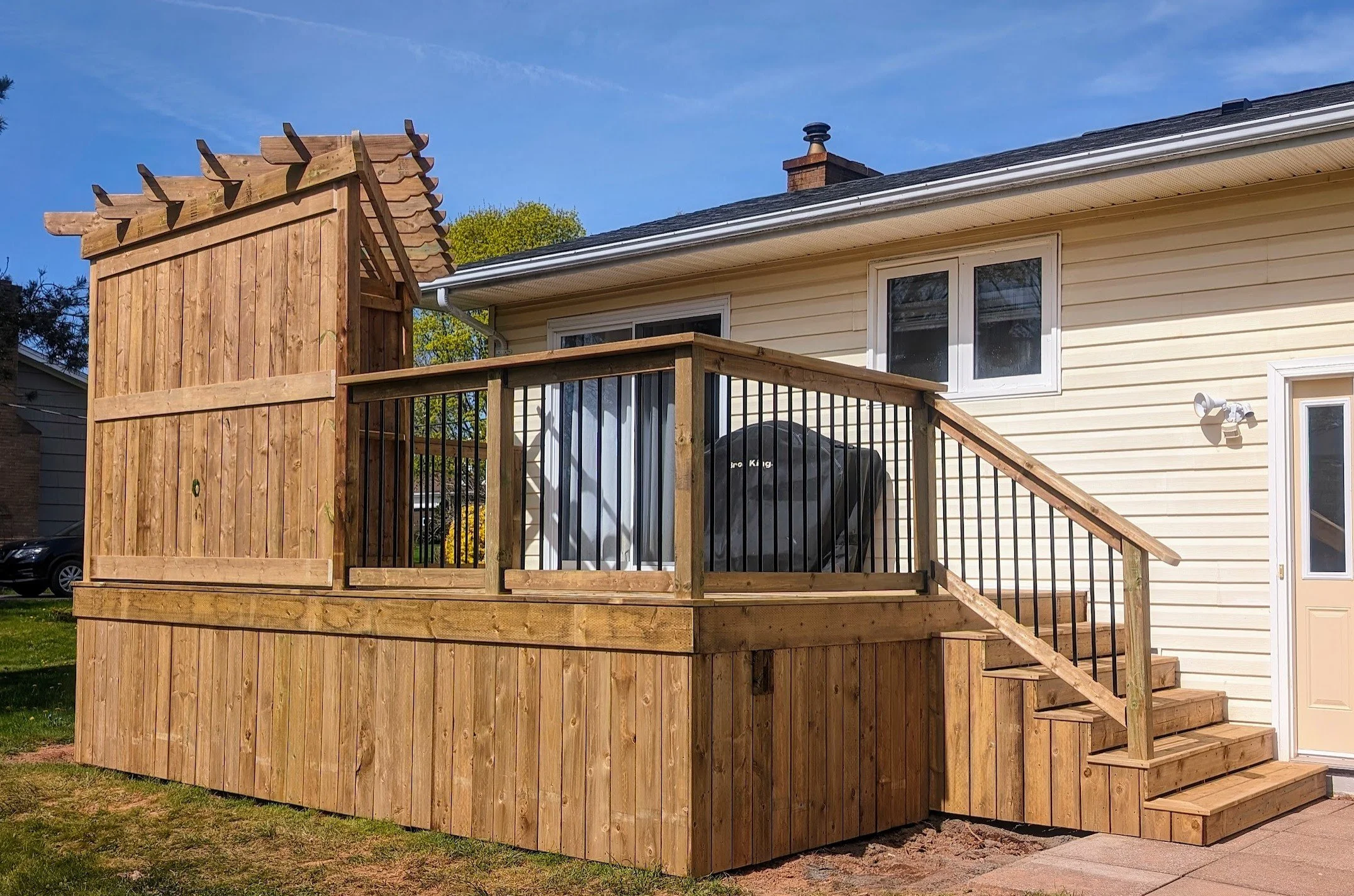 Custom design pressure treated corner wood pergola on deck with black aluminum railings and stairs built for a homeowner in Charlottetown, PEI 