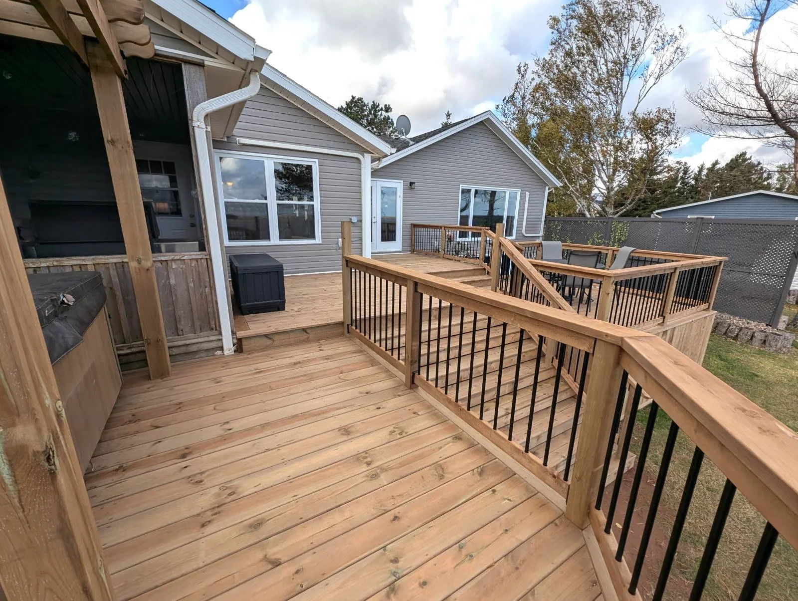 Custom built, pressure treated wooden multi-level deck with pergola over the hot tub,  black aluminum railings, under deck storage and inset stairs built for a home owner in West Covehead, PEI