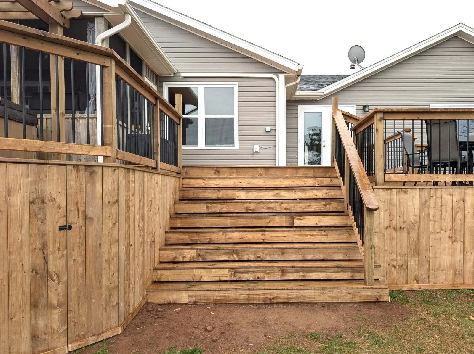 Custom built, pressure treated wooden multi-level deck with pergola over the hot tub,  black aluminum railings, under deck storage and inset stairs built for a home owner in West Covehead, PEI