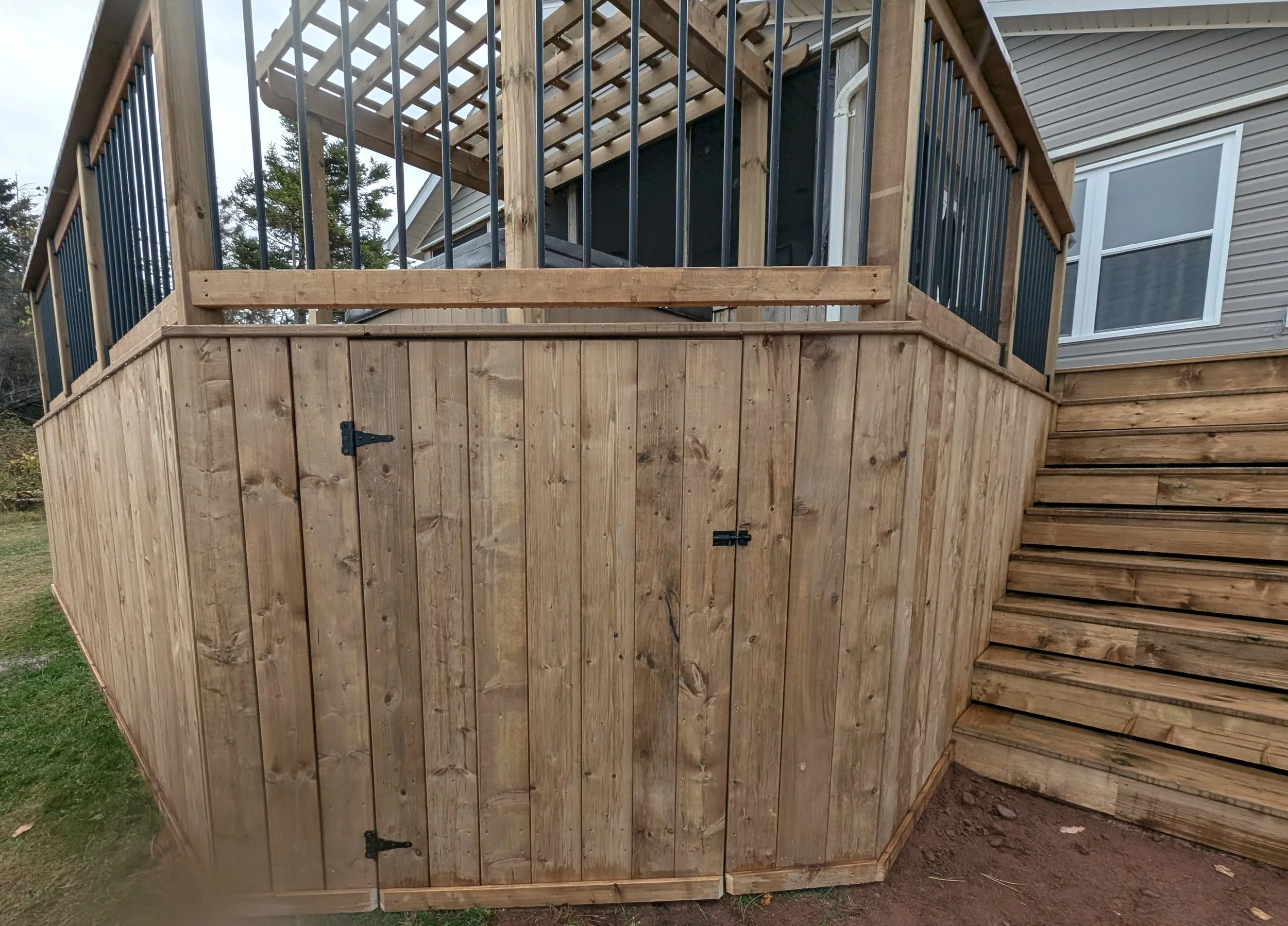 Custom design pressure treated wood pergola on multi-level deck with black aluminum railings, stairs and under deck storage built for a homeowner in West Covehead, PEI 