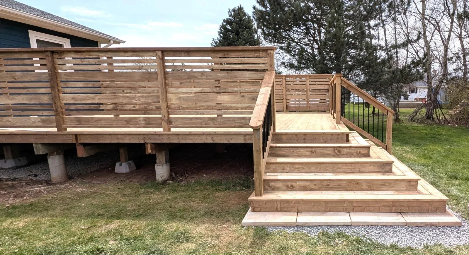 Custom built, pressure treated, wooden deck with wood privacy & black aluminum railings, and cascading stairs built for a homeowner in Winsloe, PEI.