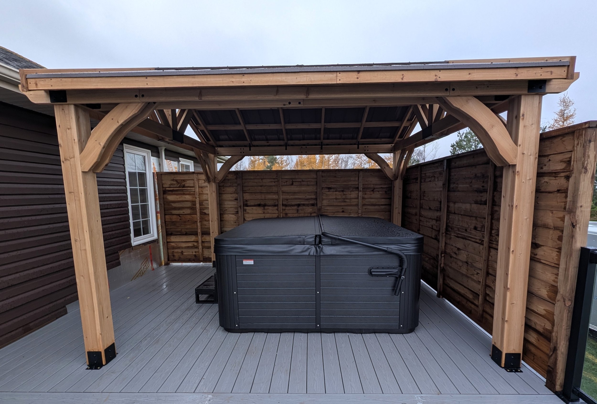 Wood pergola hot tub enclosure with metal roof on composite deck with glass & black aluminum railings built for a homeowner in Cornwall, PEI 