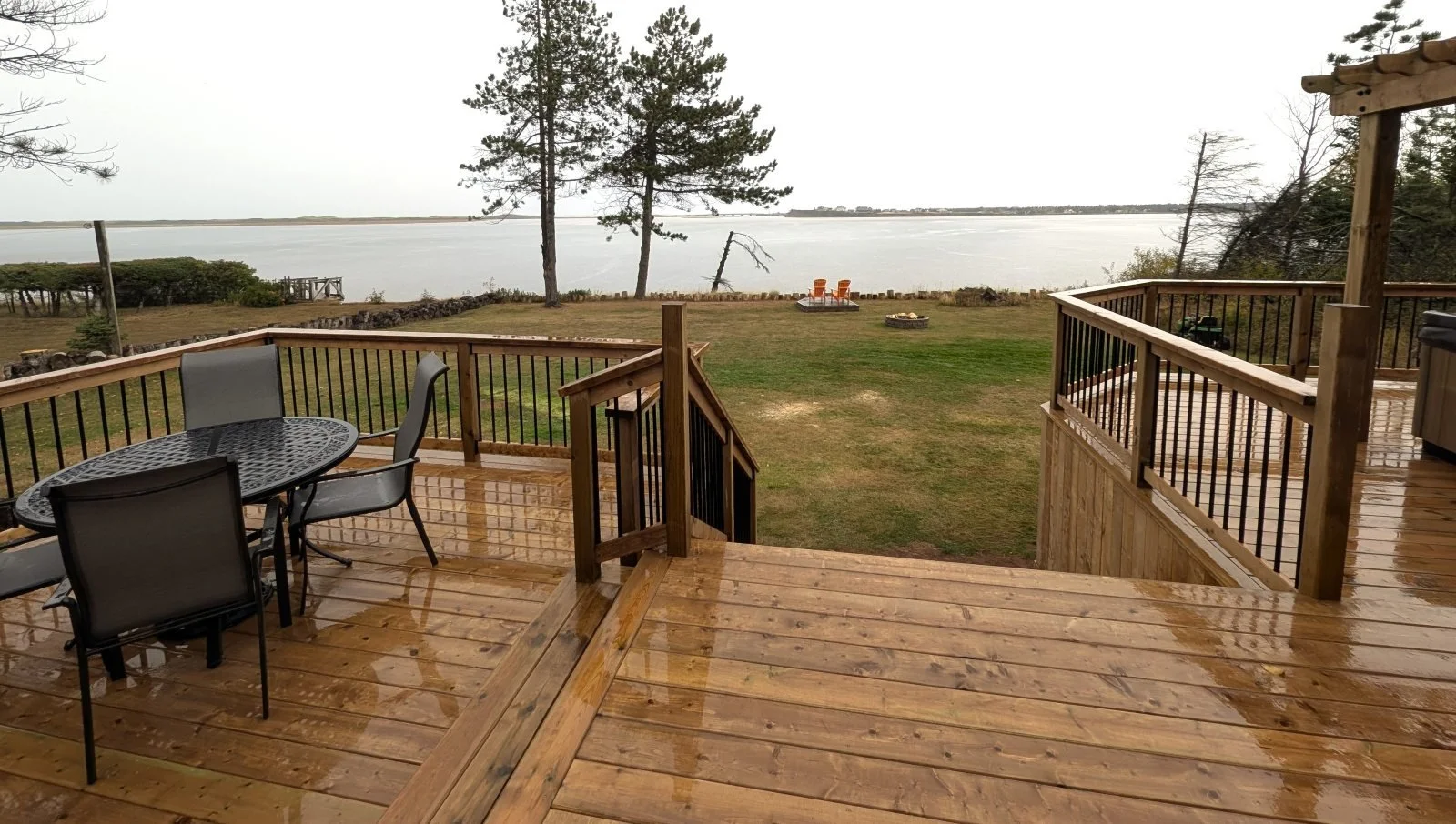 Custom built, pressure treated wood multi-level deck with pergola over the hot tub and seperate dining area, overlooking the shores of PEI,  black aluminum railings, and inset stairs built for a home owner in West Covehead, PEI