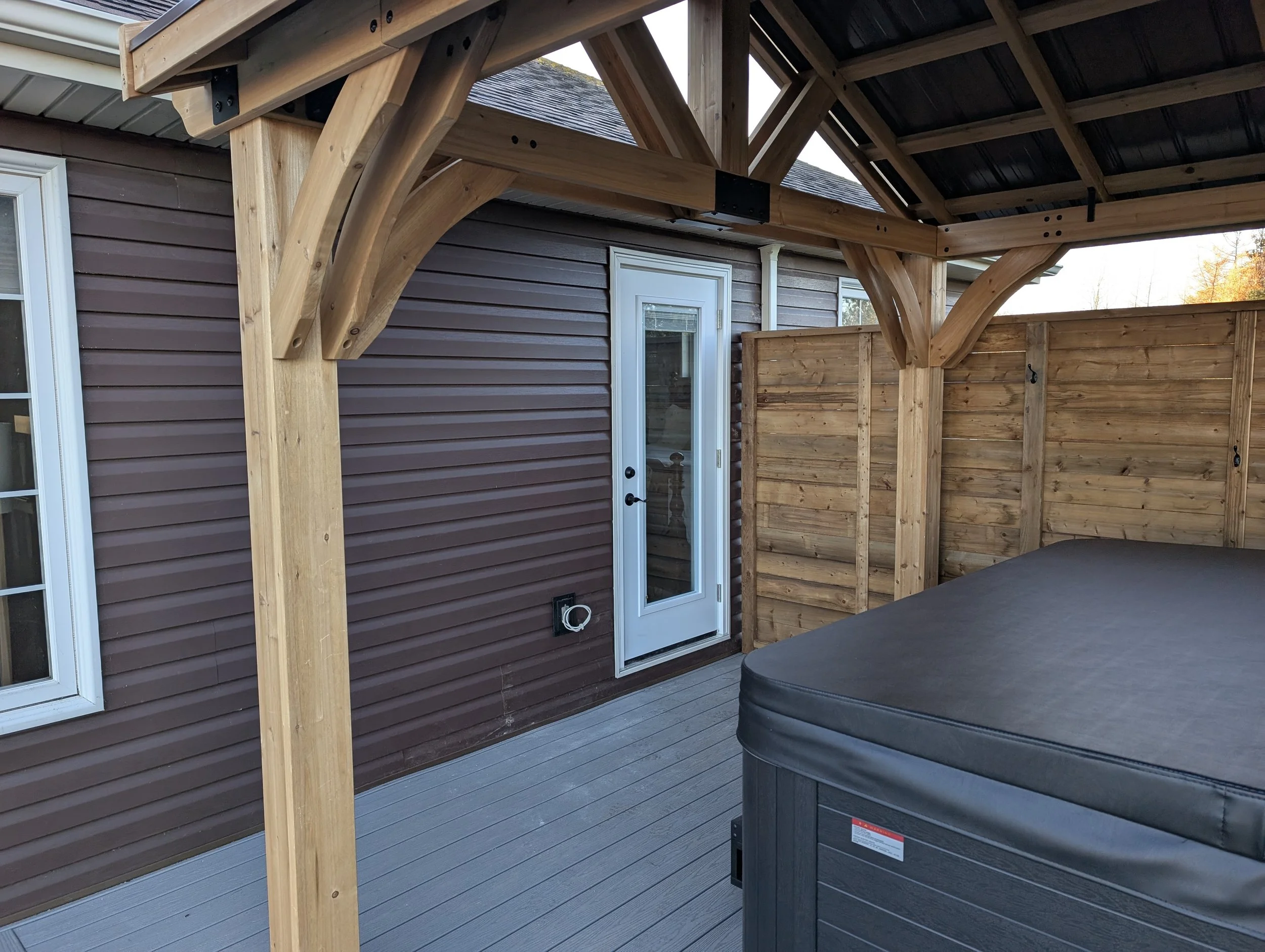 Wood pergola hot tub enclosure with metal roof on composite deck with glass & black aluminum railings built for a homeowner in Cornwall, PEI 
