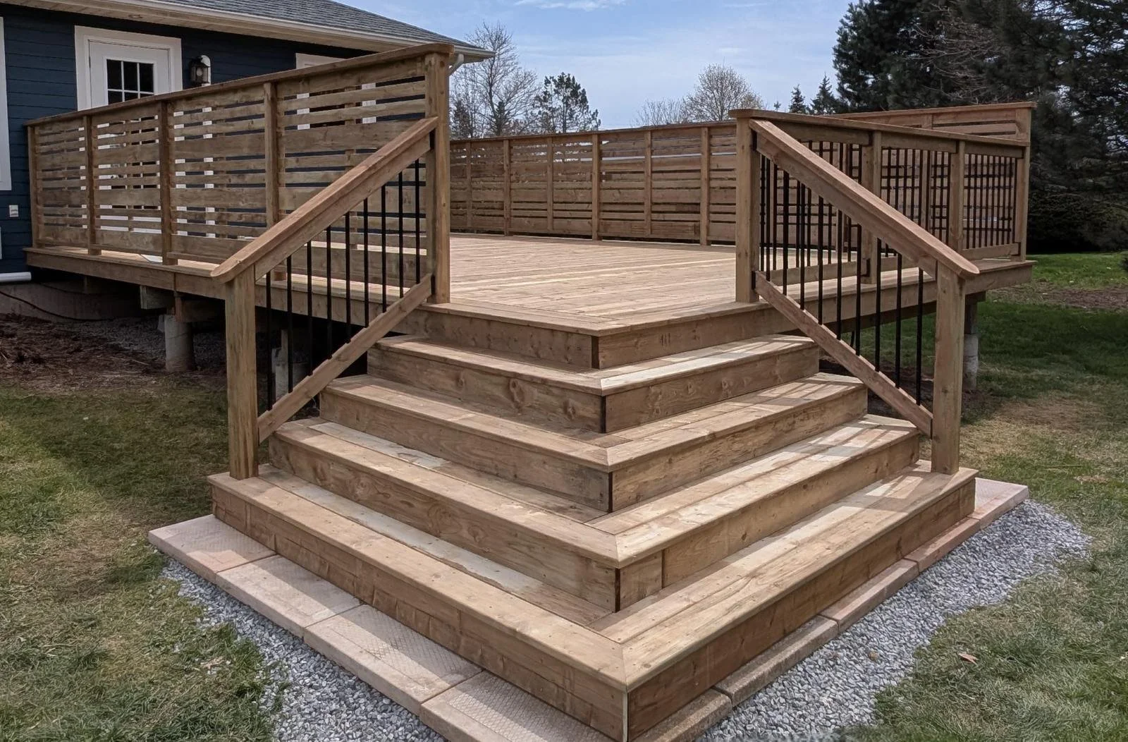 Custom built, pressure treated, wooden deck with wood privacy & black aluminum railings, and cascading stairs built for a homeowner in Winsloe, PEI.