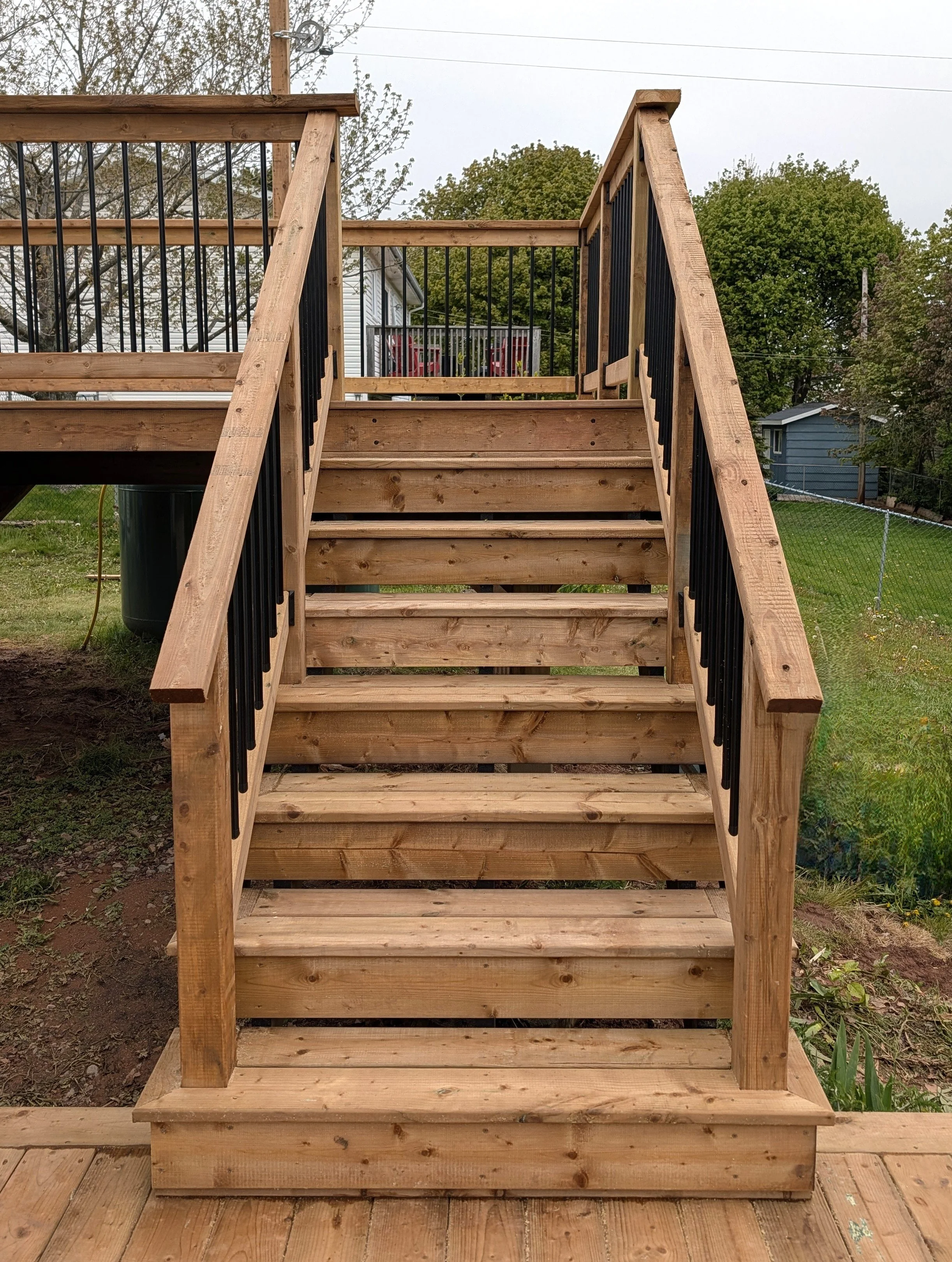 Custom design and built, pressure treated wooden deck with stairs, black aluminum railing and bottom landing built for homeowner in Charlottetown, PEI