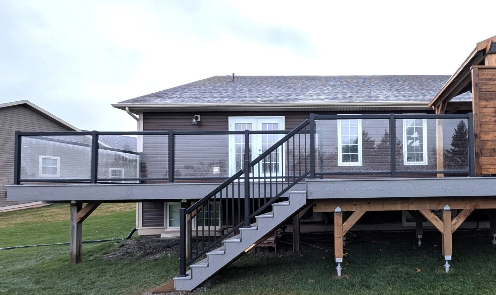 Grey composite deck with glass and black aluminum railings, gazebo and privacy walls for hot tub enclosure built for a homeowner in Cornwall, PEI