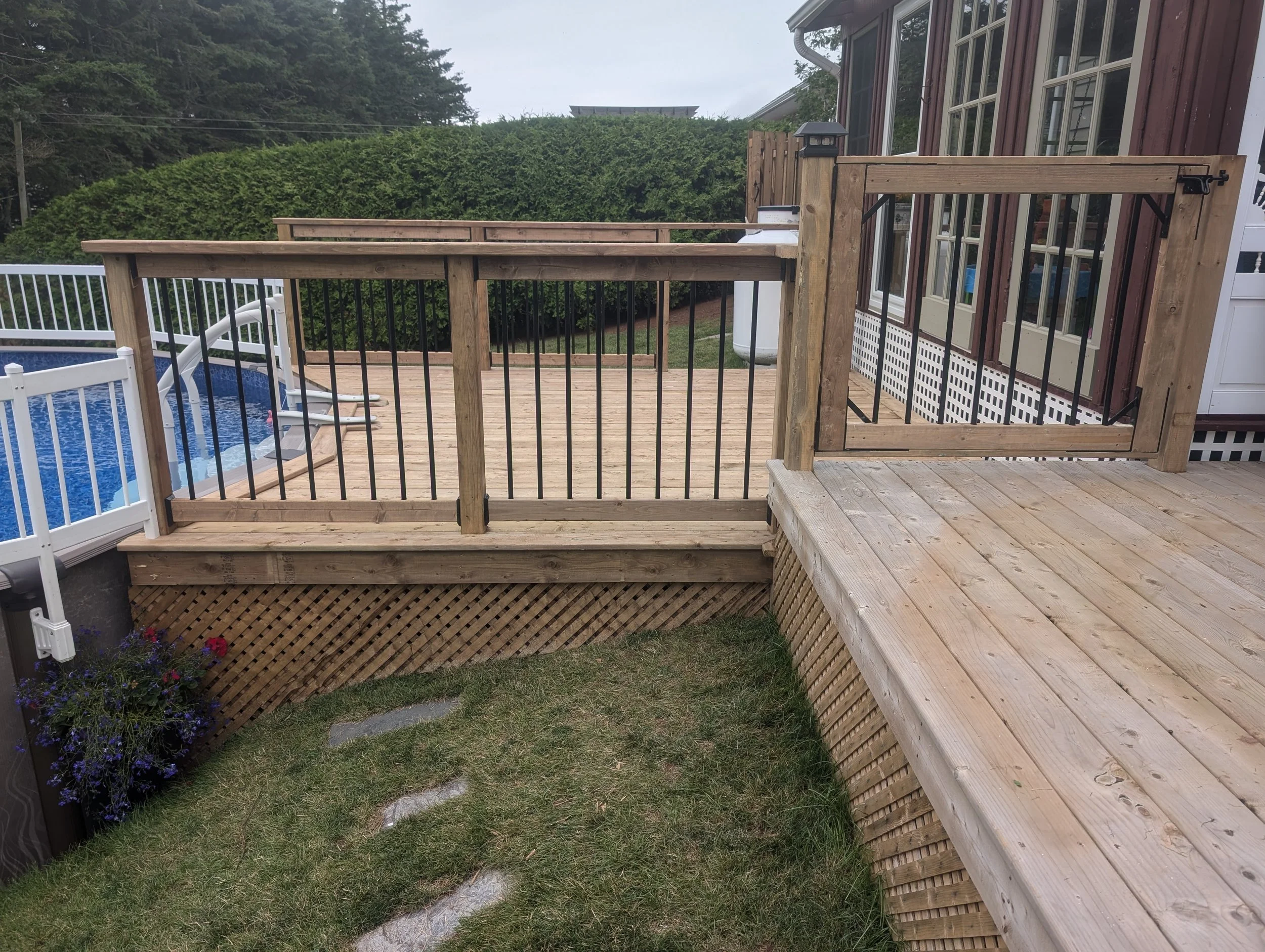 Custom built, pressure treated wooden deck with black aluminum railings, safety gate and stairs for pool, built for a home owner in Kensington, PEI