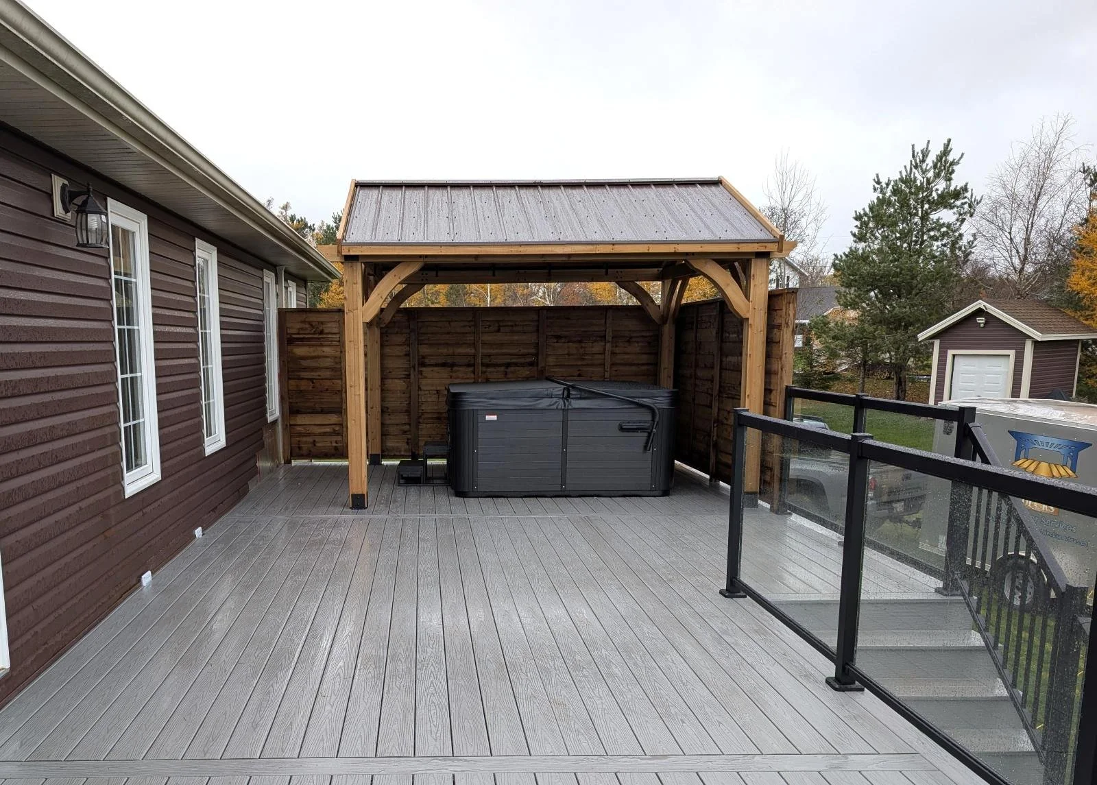 Grey composite deck with glass and black aluminum railings, gazebo and privacy walls for hot tub enclosure built for a homeowner in Cornwall, PEI