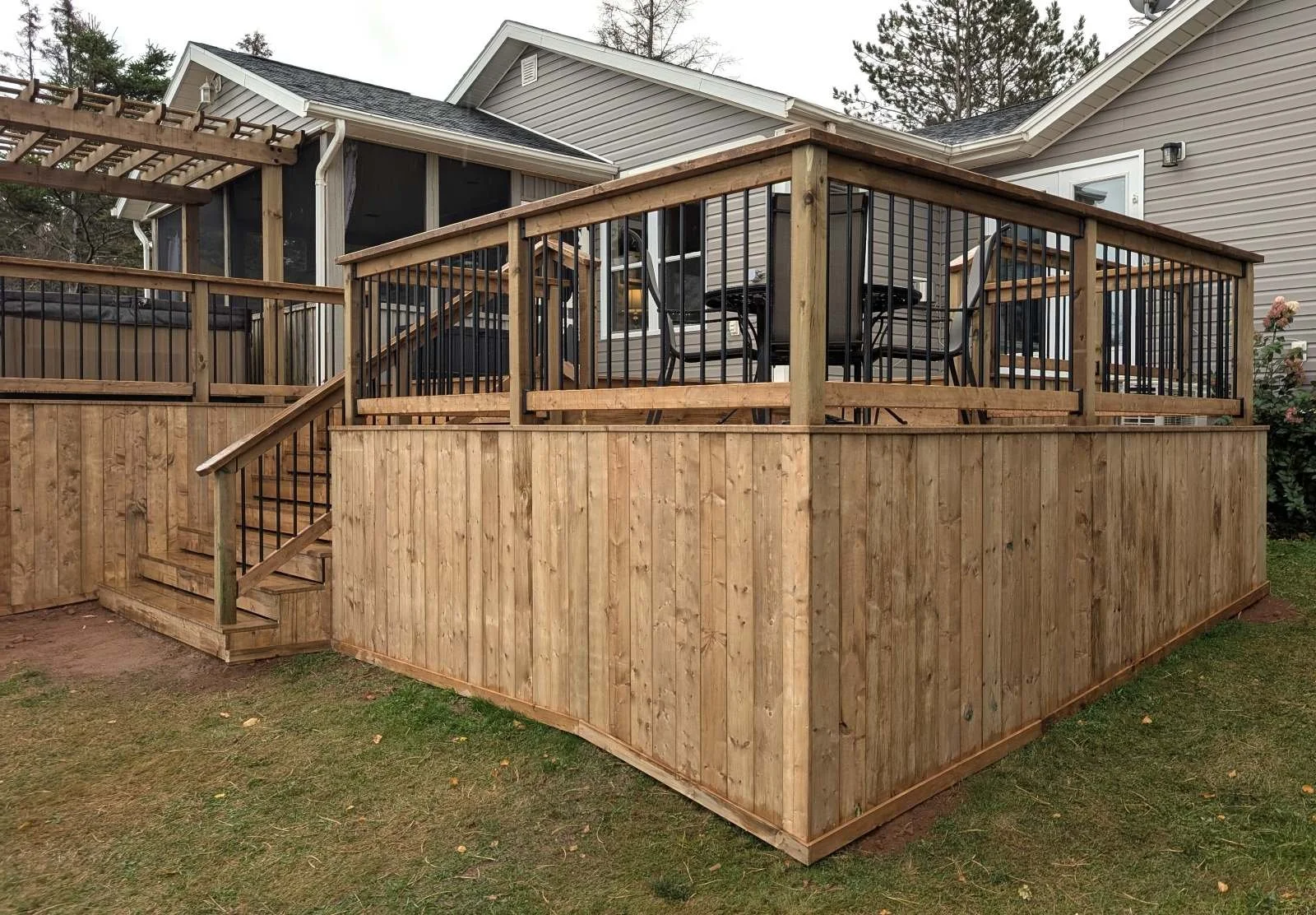 Custom built, pressure treated wooden multi-level deck with pergola over the hot tub,  black aluminum railings, under deck storage and inset stairs built for a home owner in West Covehead, PEI