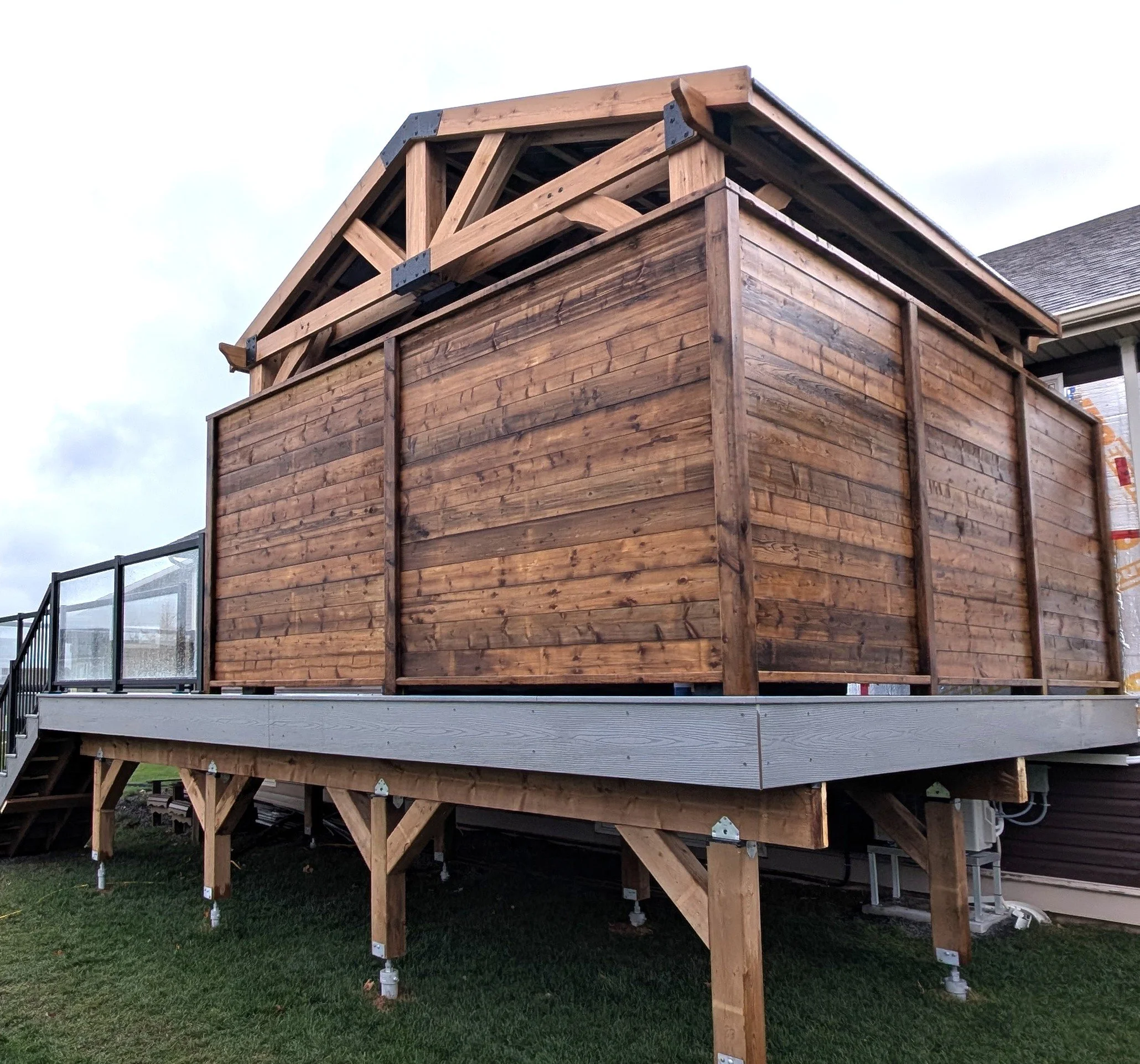 Wood pergola hot tub enclosure with metal roof on composite deck with glass & black aluminum railings built for a homeowner in Cornwall, PEI 